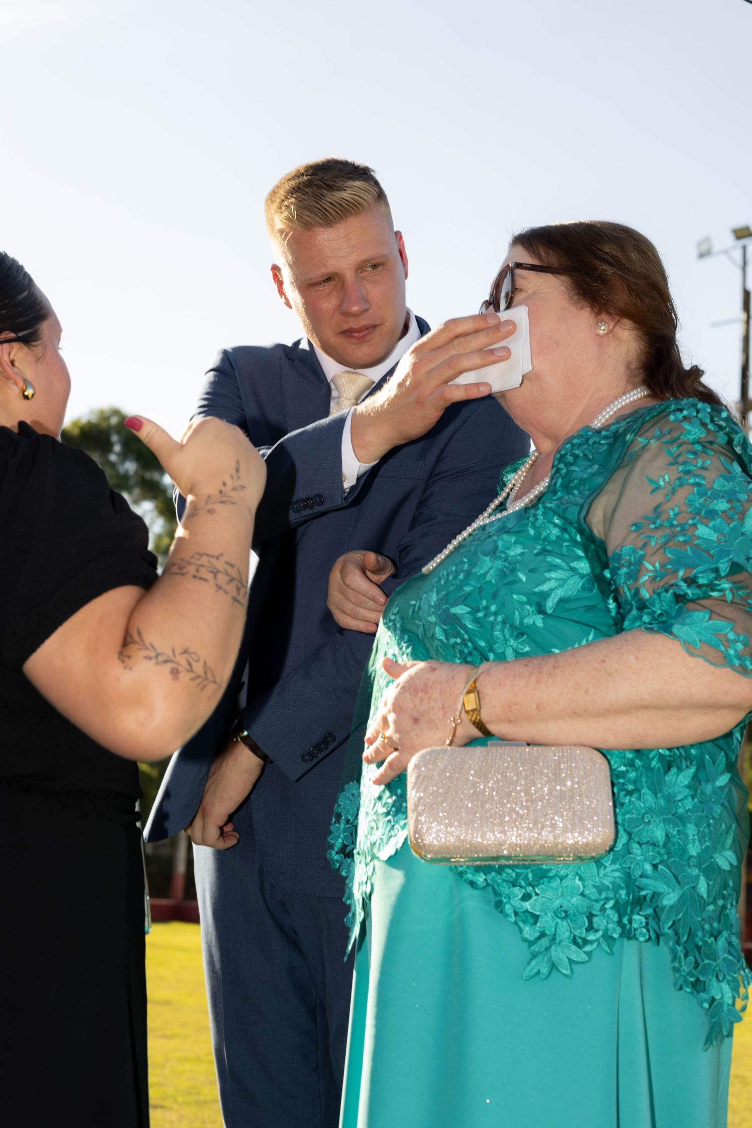 A man in a suit comforts an emotional woman in teal lace dress at a wedding outdoor ceremony.