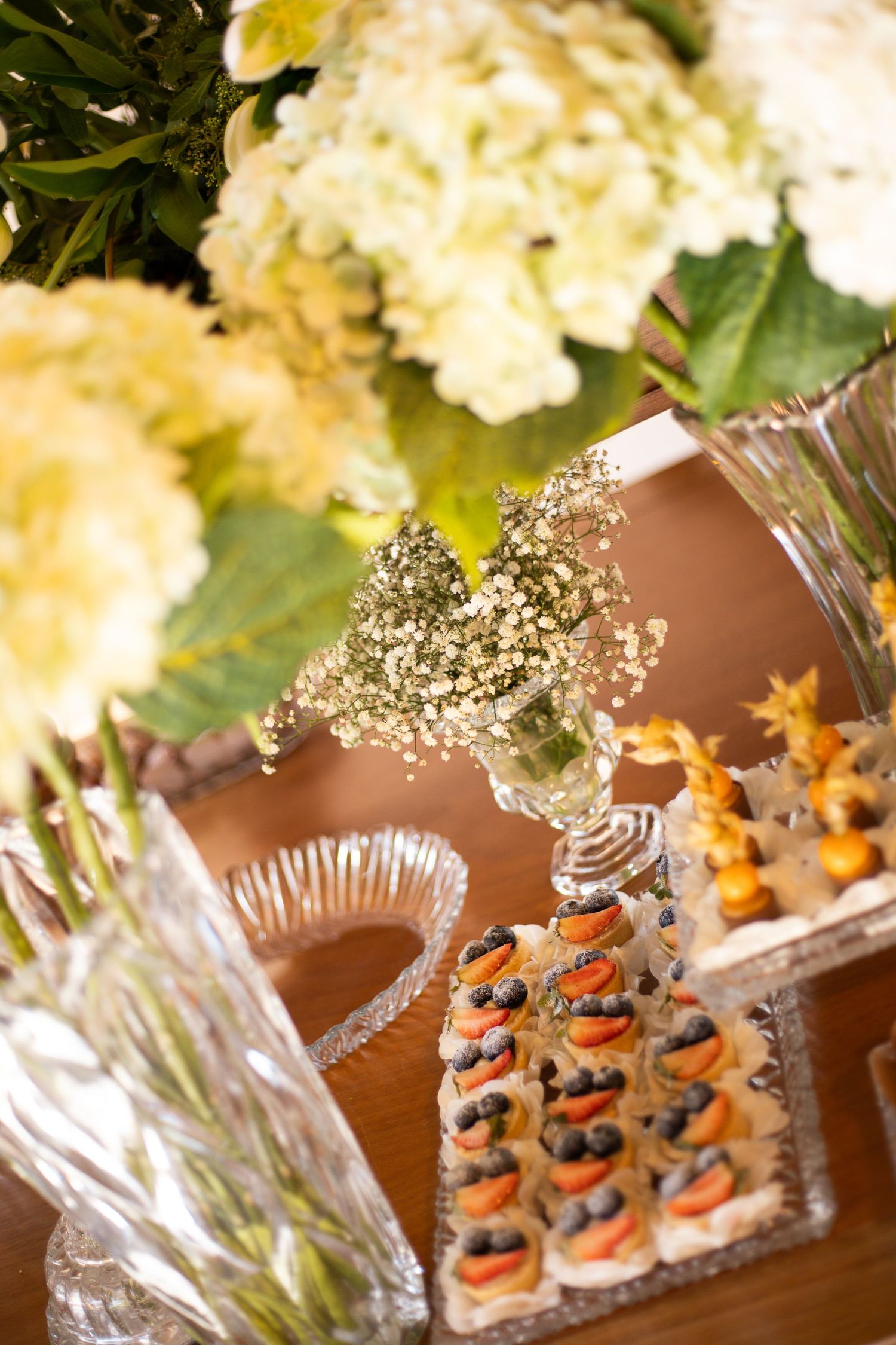 Elegant wedding reception table with white hydrangea floral arrangements and tiered crystal trays of fresh fruit tarts.