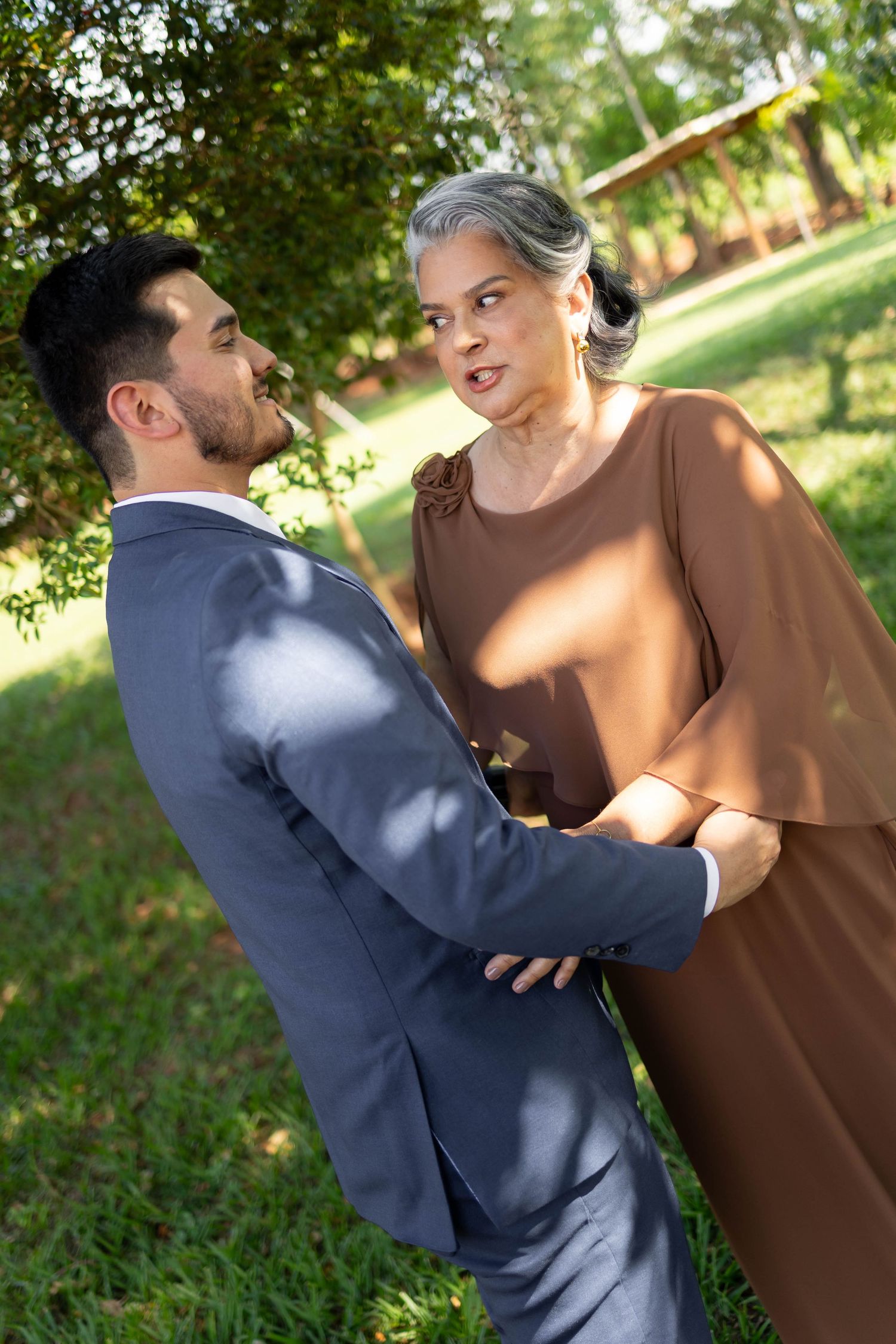 Elegant couple in formal attire sharing a romantic moment outdoors in a lush green park setting.