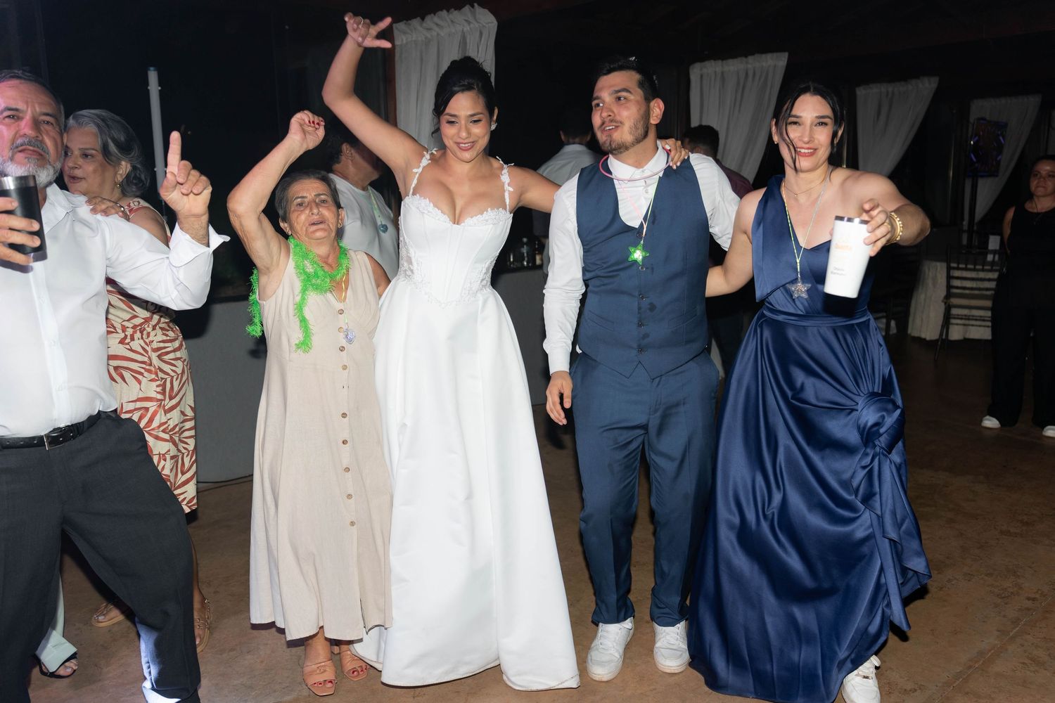 Bride and groom celebrate with guests on wedding dance floor, bride in white gown, groom in blue suit.