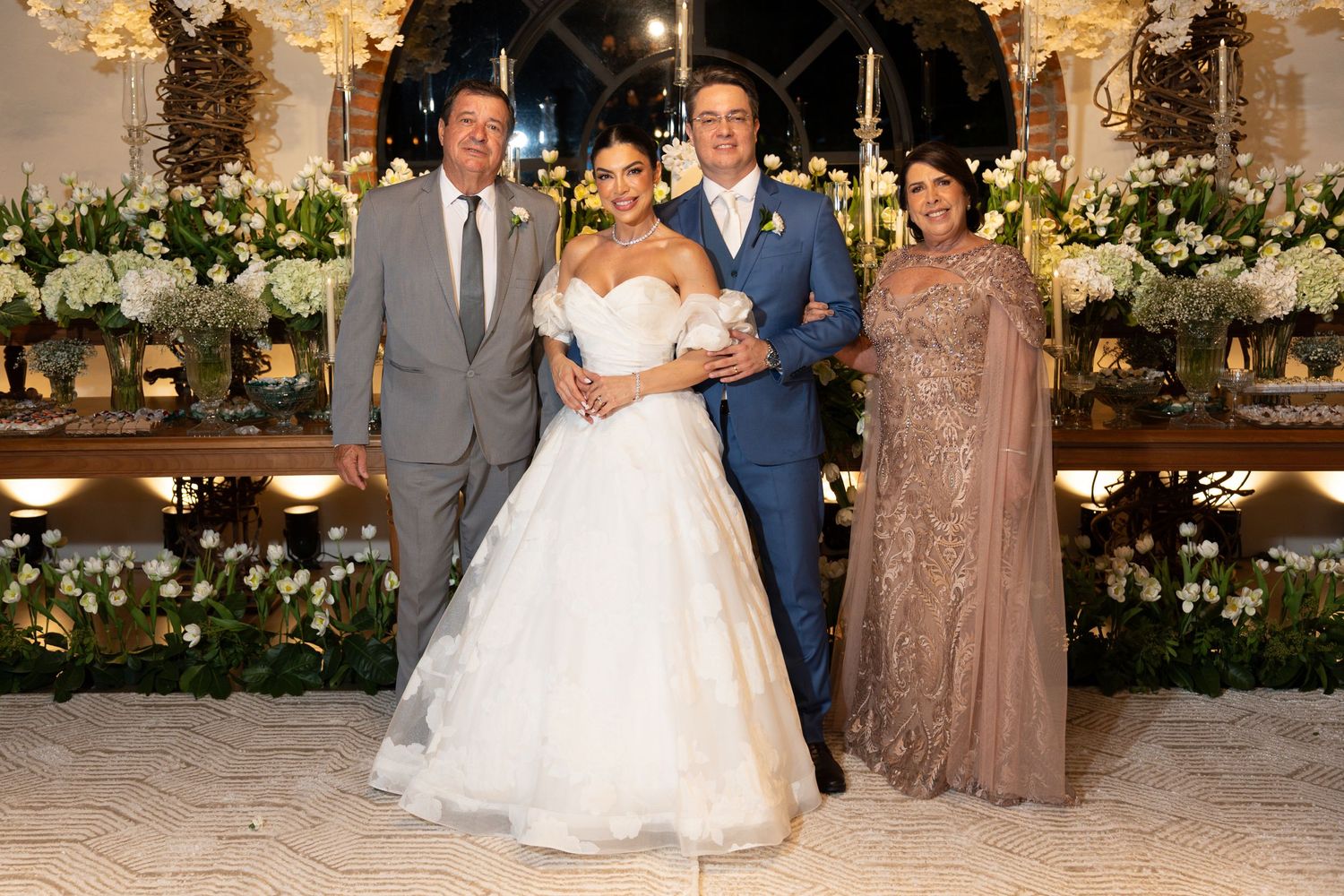 Elegant wedding ceremony with bride in white ball gown and groom in suit, posing with family amid lush floral decorations.