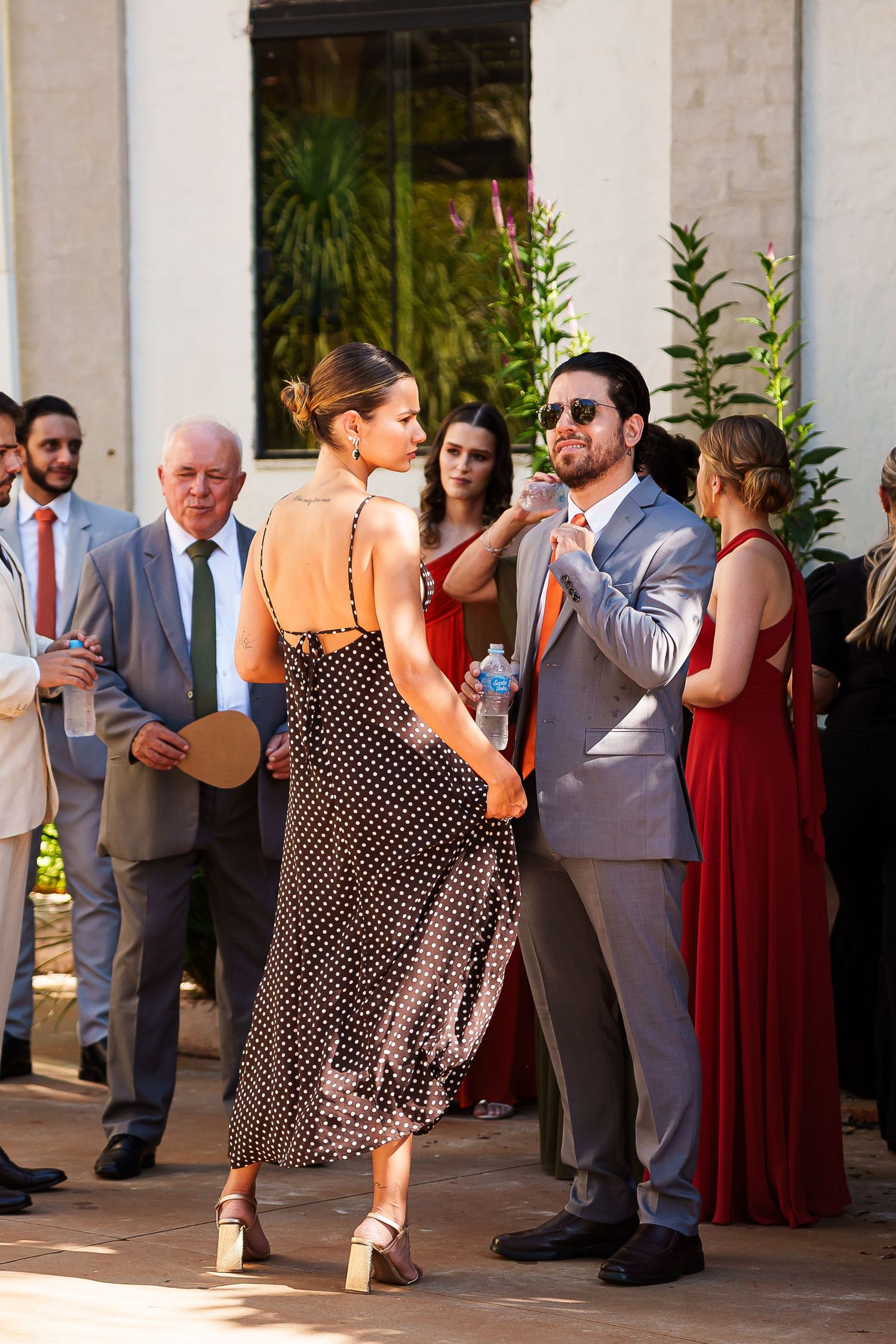 Couple dancing outdoors at a wedding reception, woman in polka dot dress, man in gray suit with sunglasses.