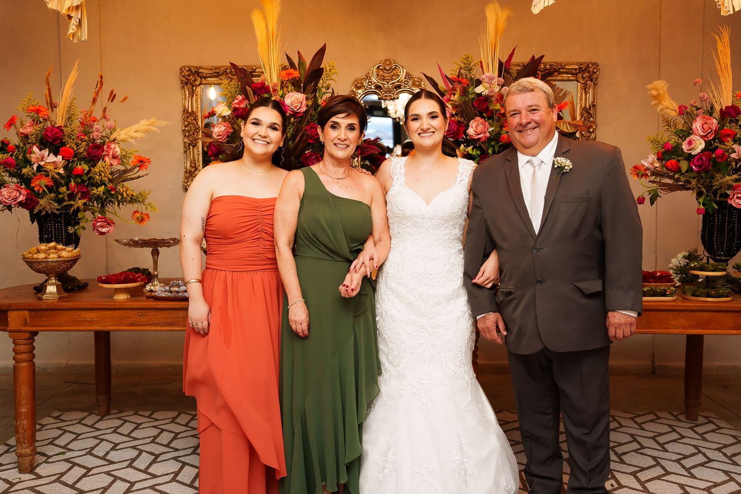 Bride in white gown poses with two bridesmaids in orange and green dresses and a man in suit at wedding reception.