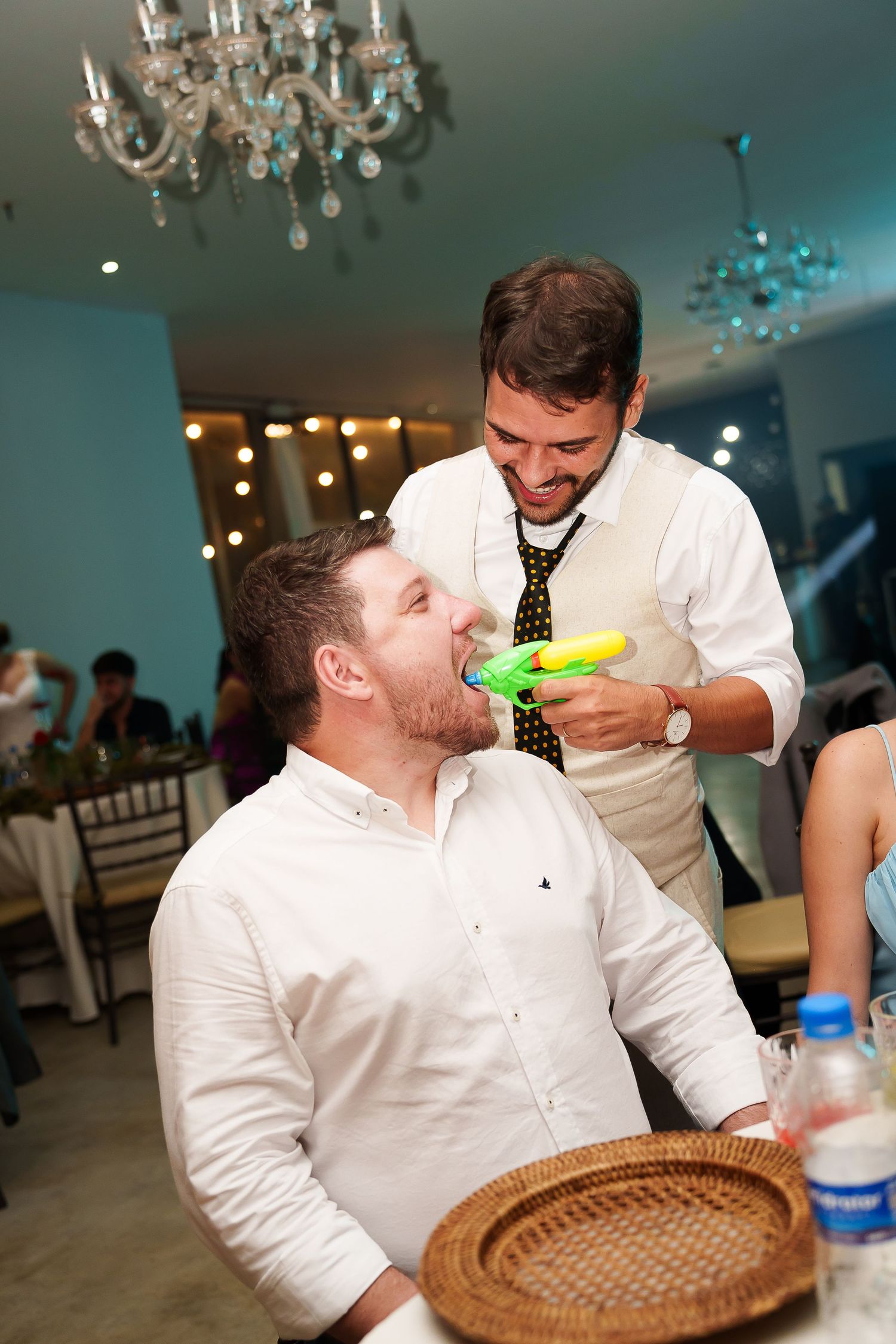 Man shoots water gun into another man's mouth at a festive indoor party event.