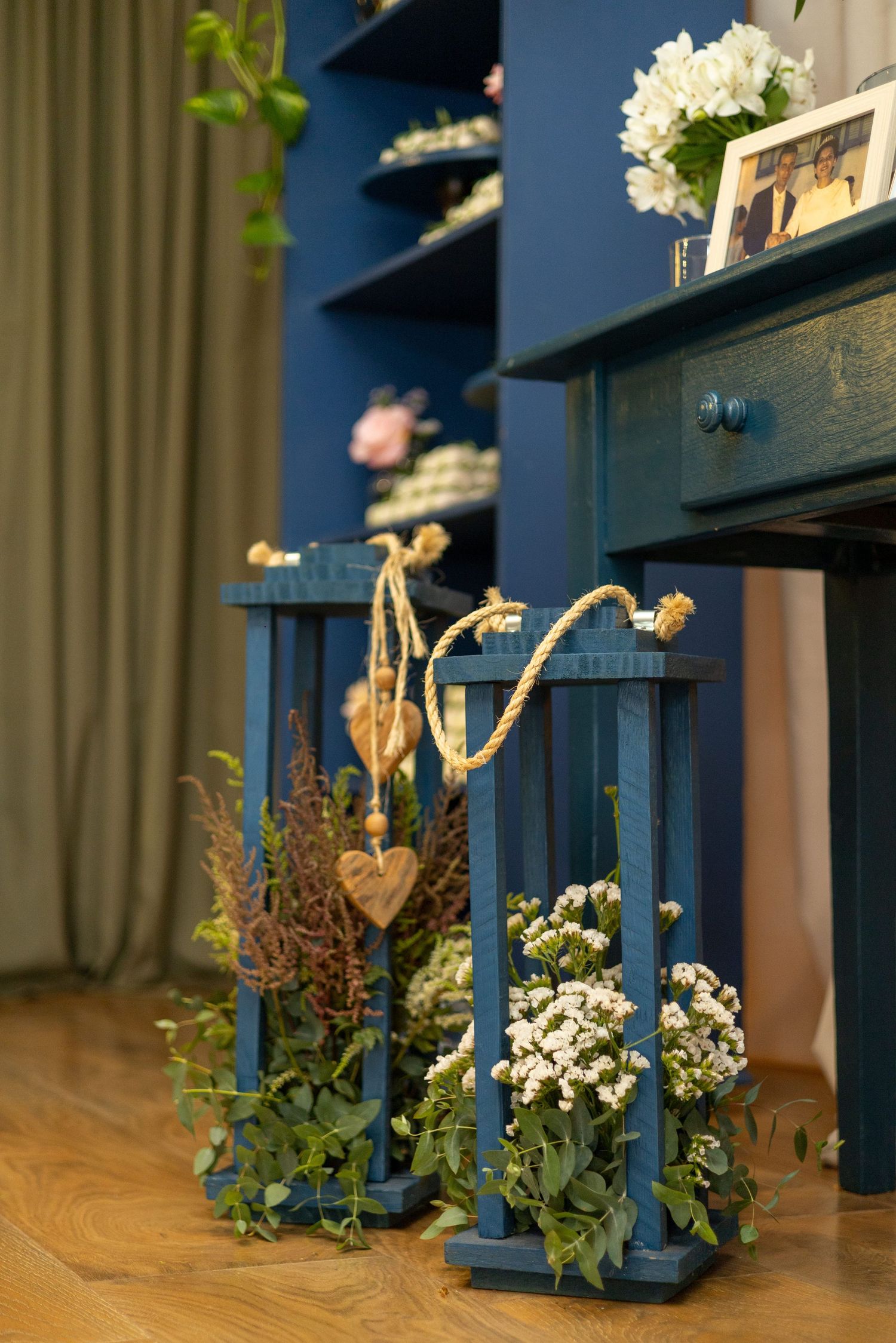 Blue wooden lanterns with white flowers and heart decorations beside a vintage blue dresser with floral arrangements.