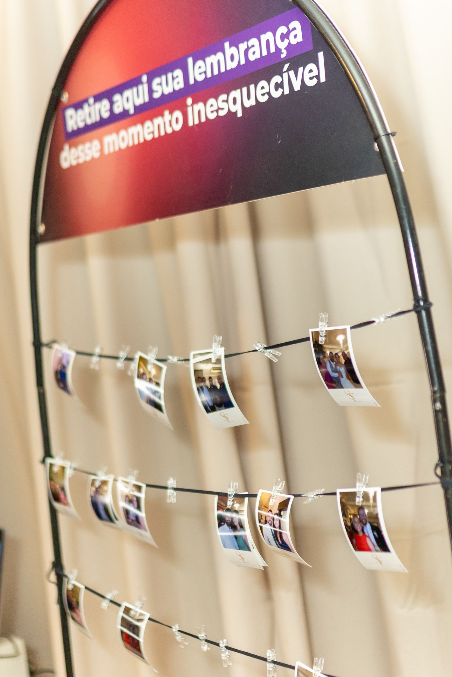Photo display stand with printed pictures clipped to strings, featuring Portuguese text sign at an event.