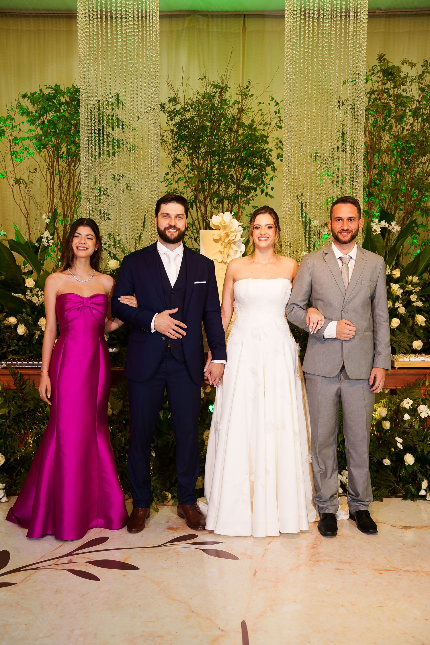 Wedding party posing elegantly, bride in white gown, groom in navy suit, bridesmaid in magenta dress, groomsman in gray suit.
