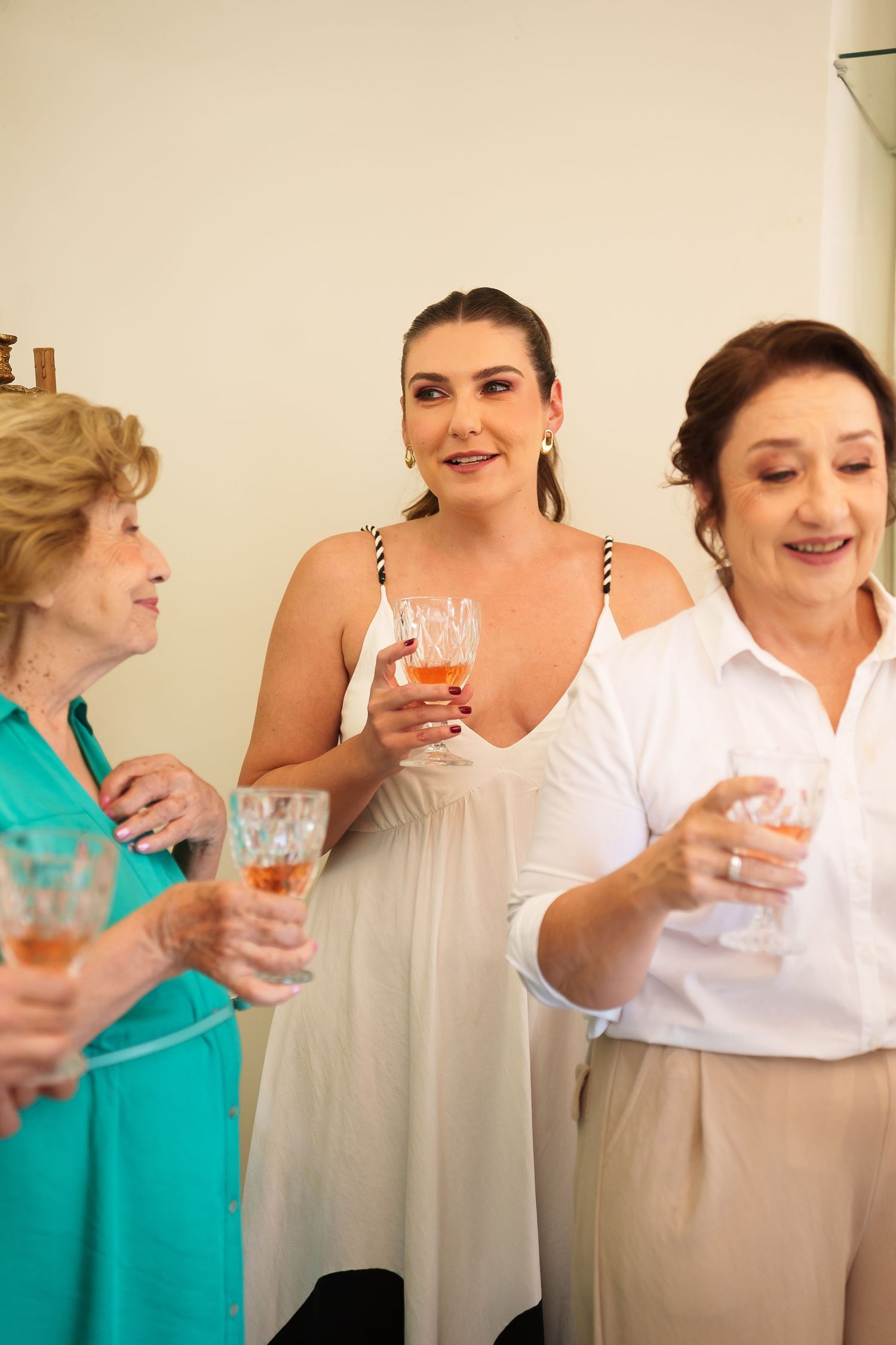 Three women smiling and holding champagne glasses at a celebration, dressed in elegant attire.