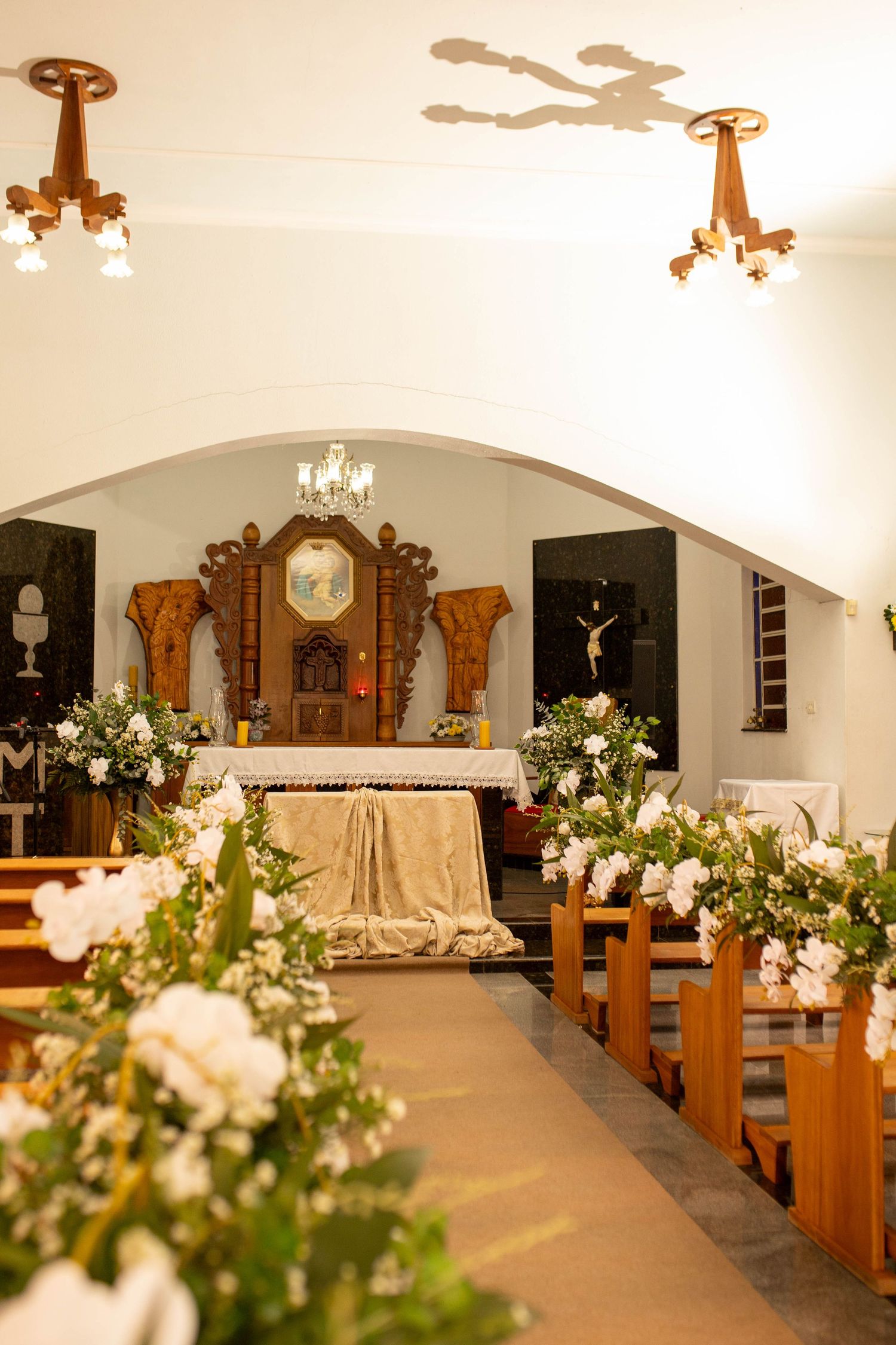 Elegant church interior decorated with white flowers along wooden pews leading to ornate altar for a wedding ceremony.