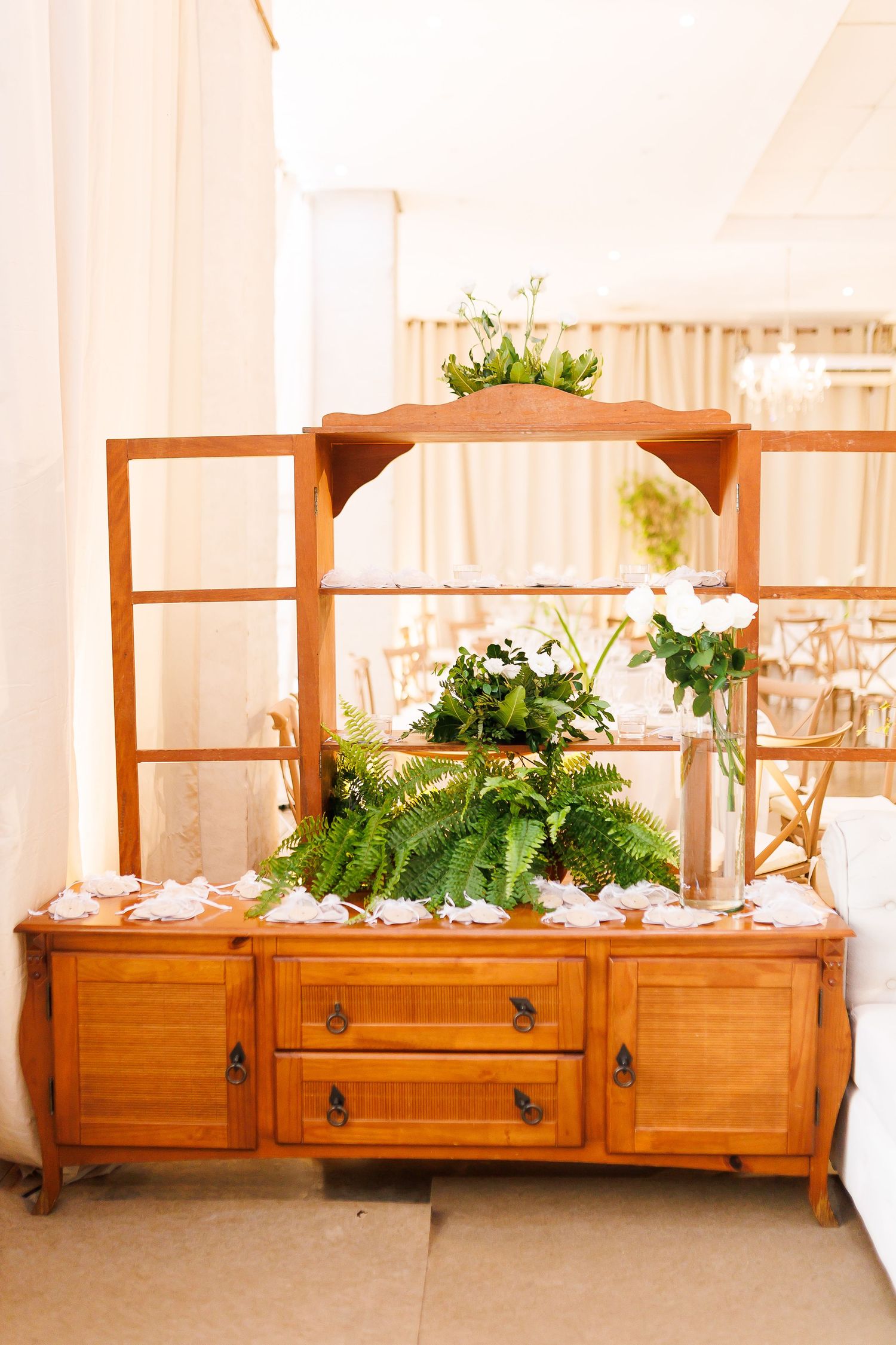 Rustic wooden dresser decorated with lush ferns and white roses, styled for an elegant wedding venue.