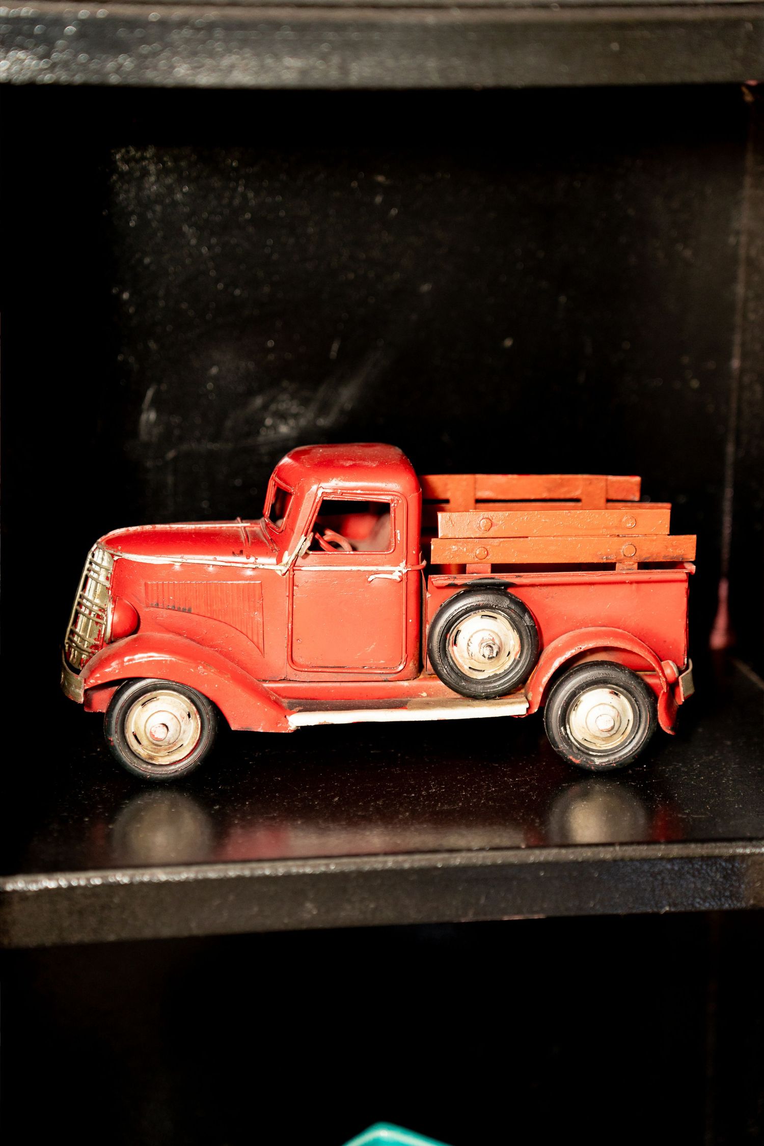 Vintage red toy pickup truck with wooden slat bed displayed on a dark shelf.