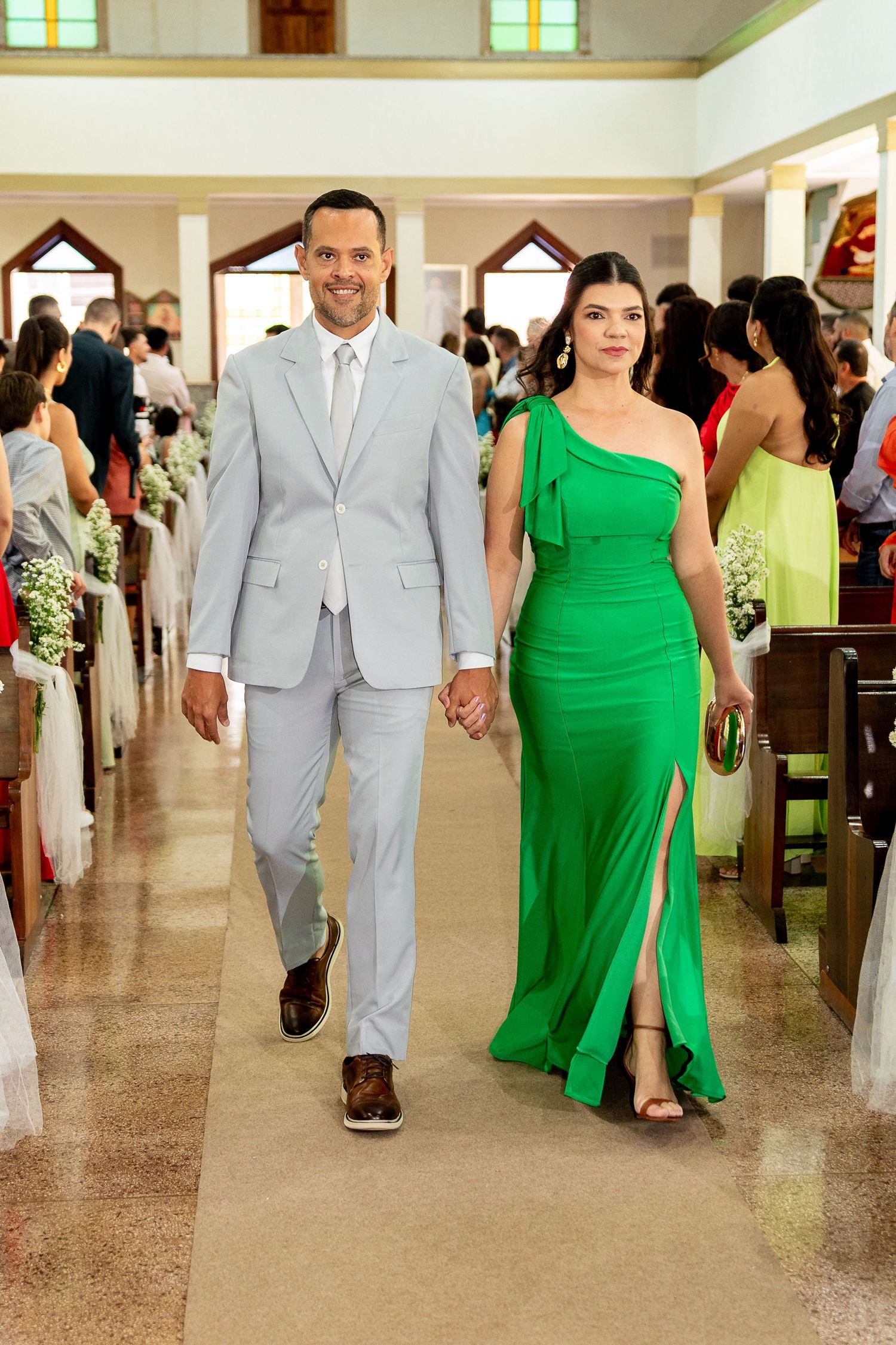 Couple walking down church aisle, man in gray suit, woman in elegant green gown, wedding ceremony.
