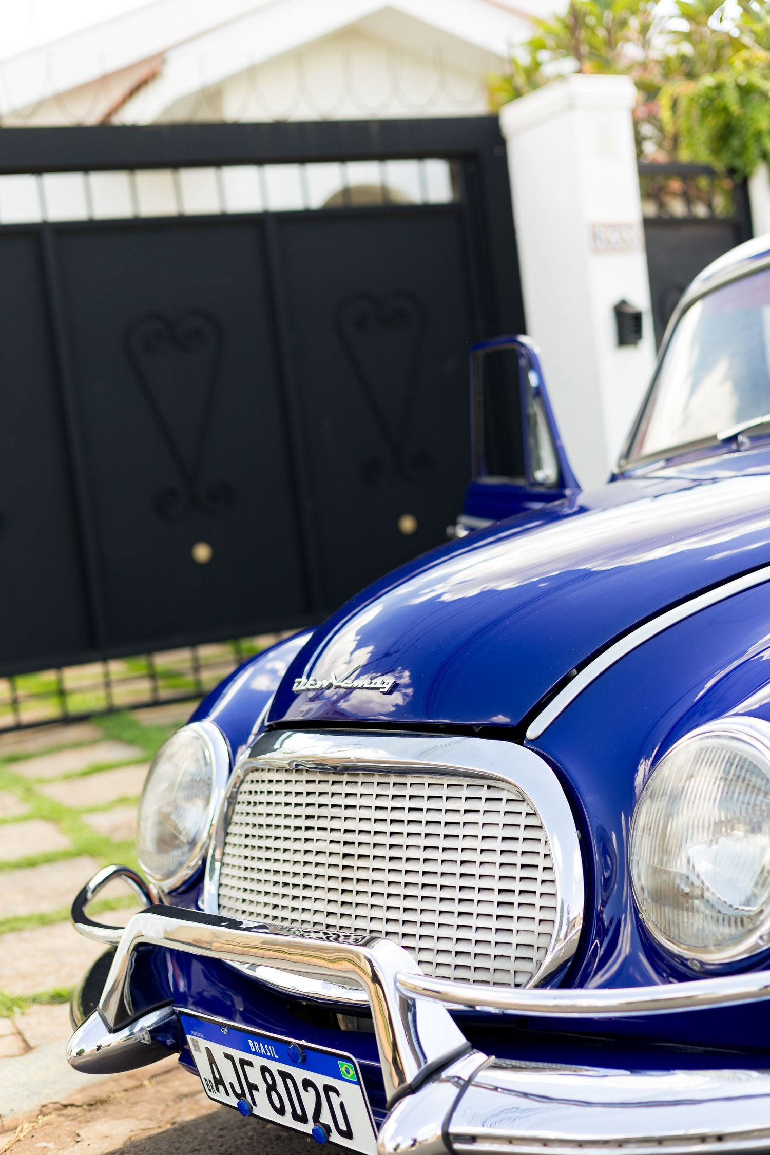 Vintage blue DKW classic car parked in driveway, showcasing chrome grille and headlights with decorative black gate behind.