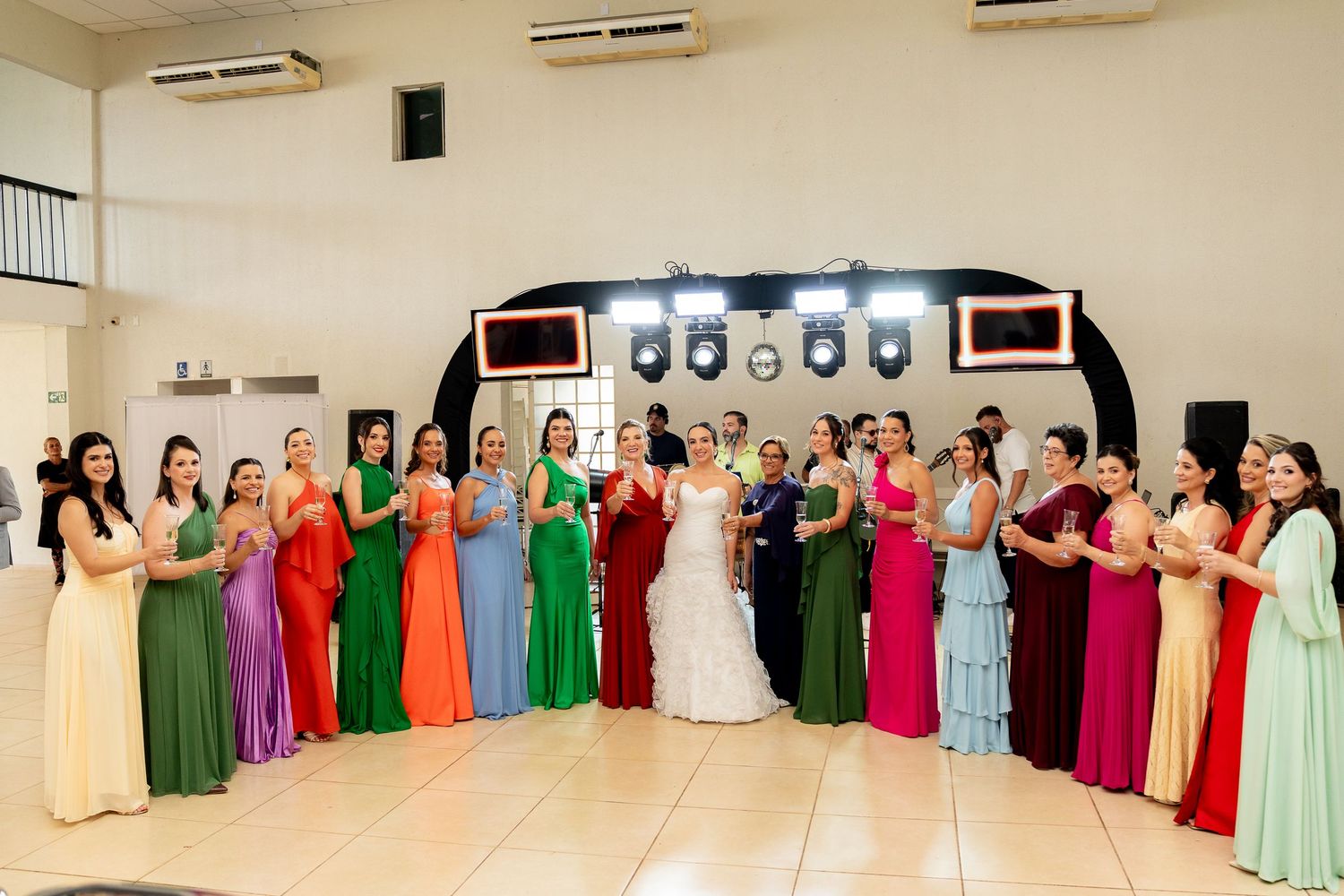 Bride in white gown poses with bridesmaids in colorful dresses at elegant wedding reception hall.