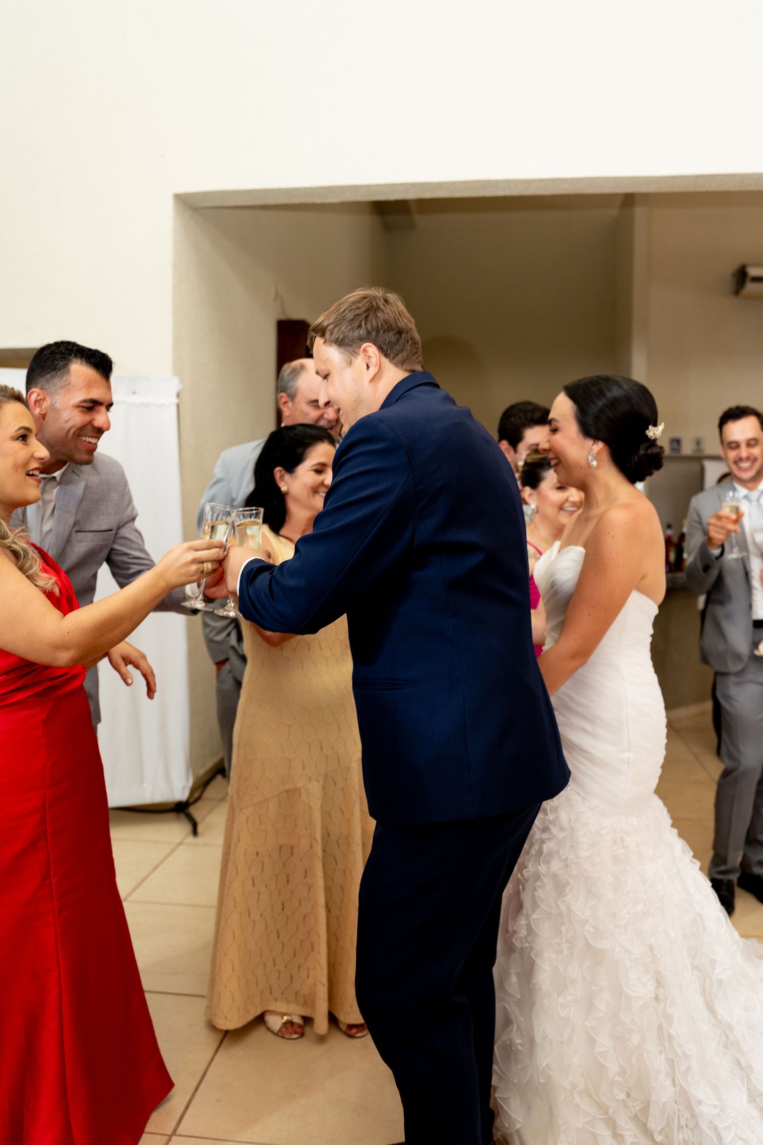 Bride and groom share a champagne toast with guests at their wedding reception, surrounded by smiling family and friends.