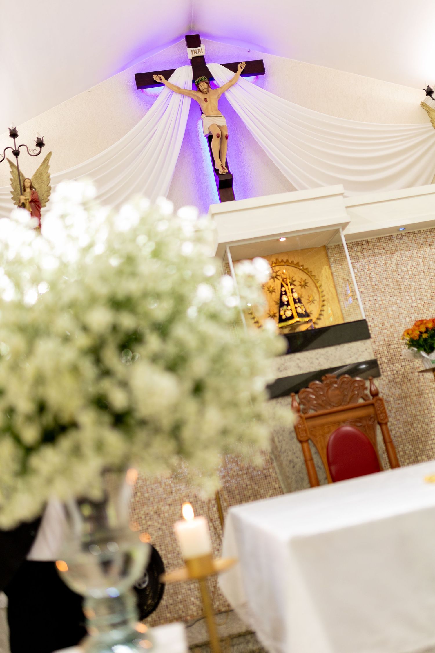 Catholic church altar with crucifix, white floral arrangements, candles, and golden religious decor during a wedding ceremony.