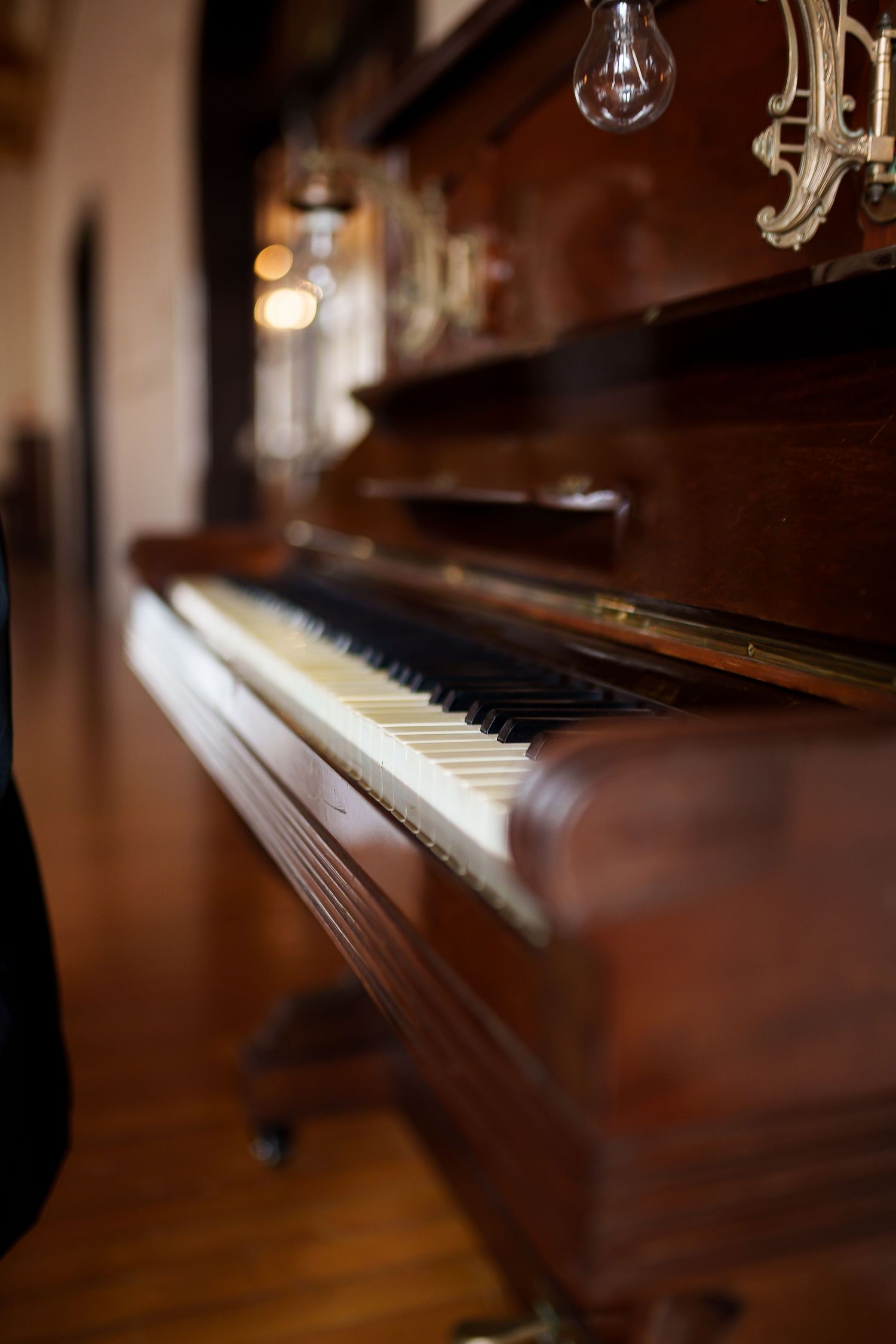 Vintage upright piano with ivory keys and ornate wood finish, adorned with decorative candelabra and Edison bulbs.
