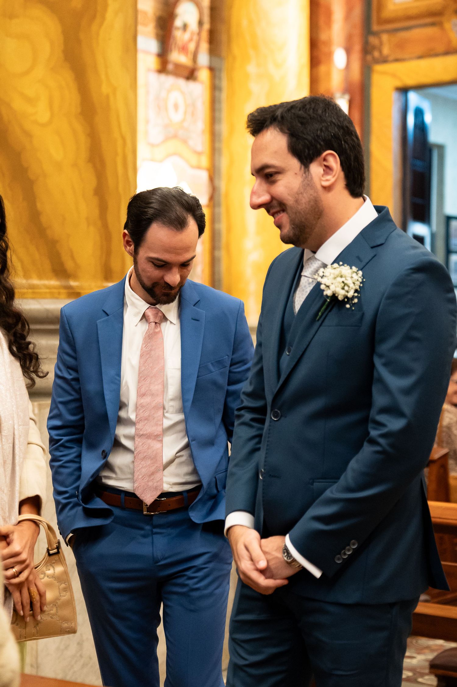 Two men in blue suits share a joyful moment at a wedding ceremony, one wearing a boutonniere.