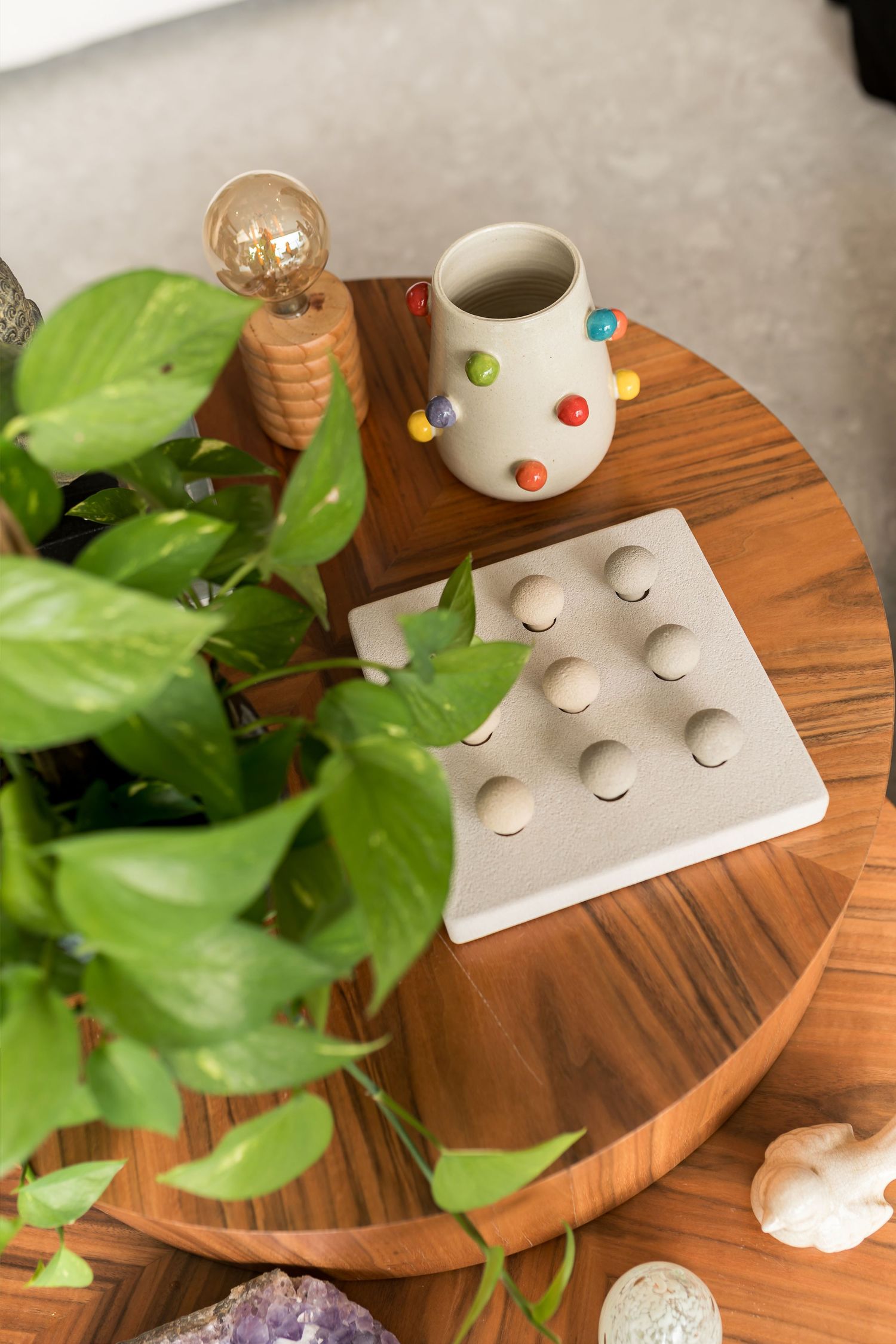 Round wooden coffee table with a polka dot vase, geometric tray, Edison bulb lamp, pothos plant, and amethyst crystal decor.