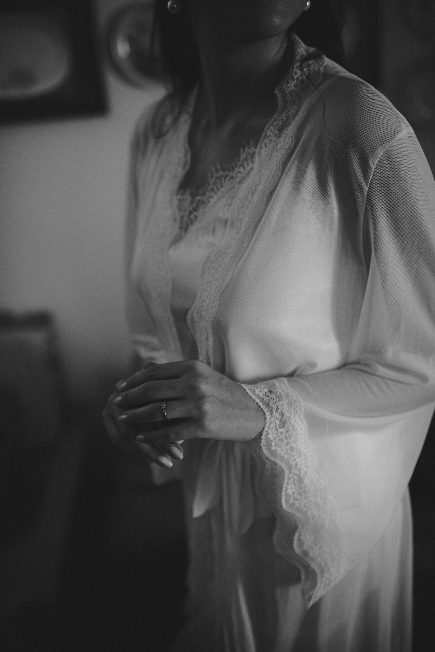 Black and white photo of a bride in a lace-trimmed silk robe adjusting her outfit before her wedding ceremony.