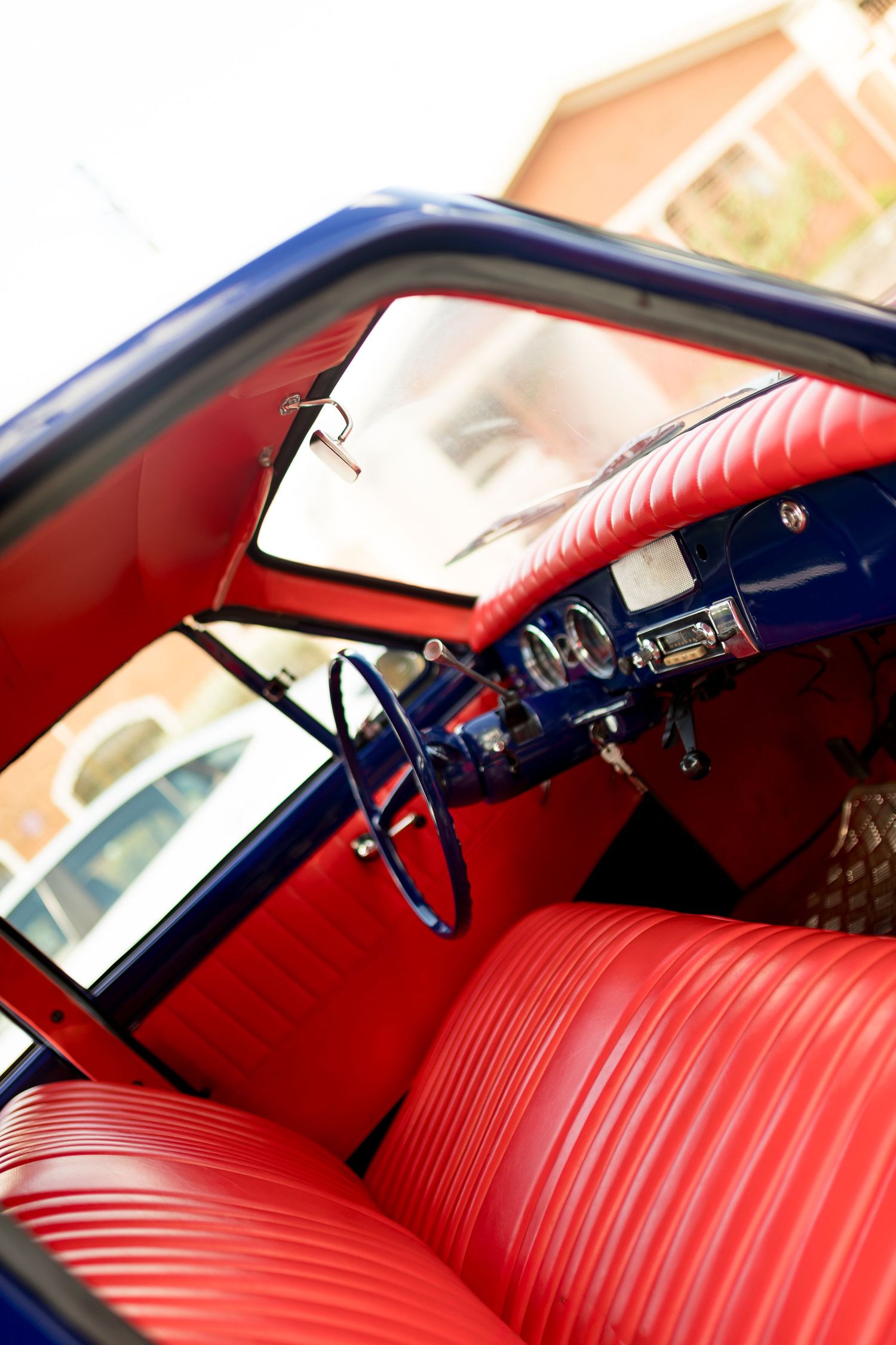 Vintage classic car interior with vibrant red leather seats and blue dashboard, steering wheel visible, retro style.