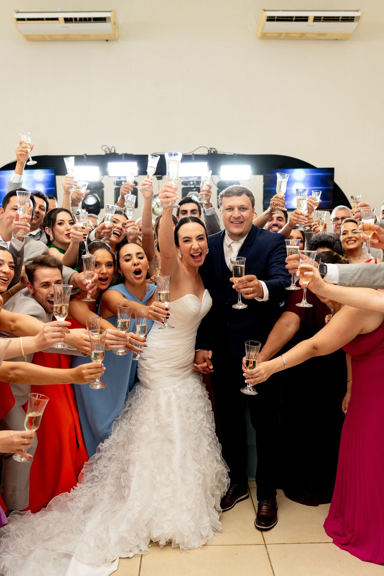 Bride and groom celebrate with wedding guests raising champagne glasses in a joyful indoor reception toast.