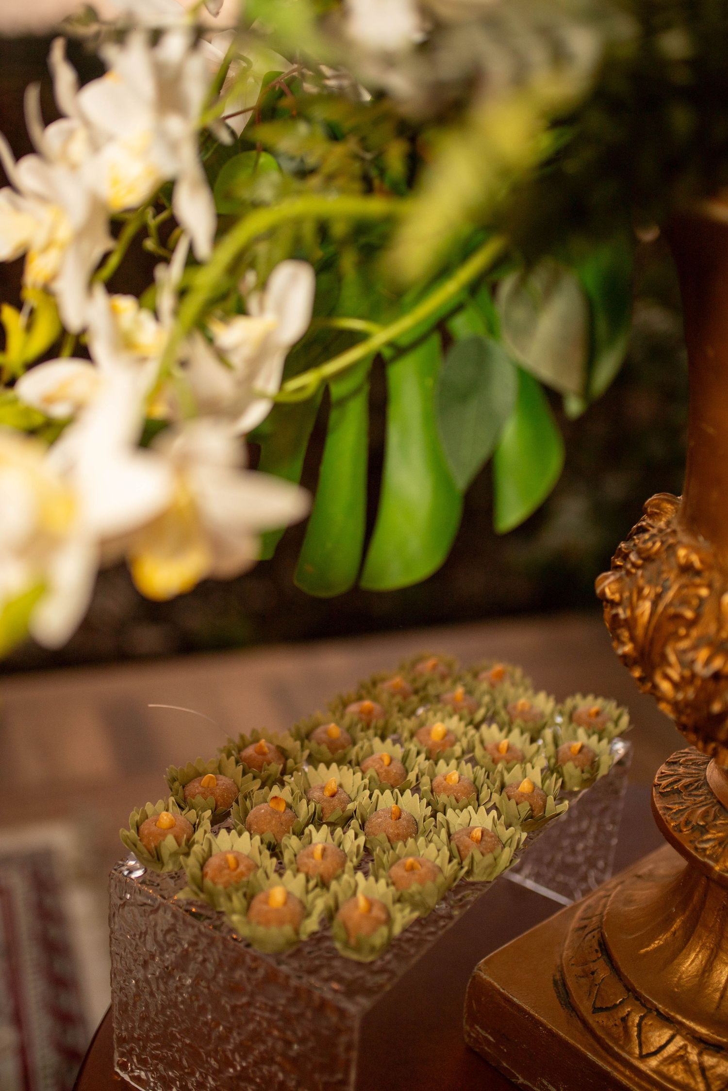 Elegant appetizer display with green herb-topped bites on crystal tray, white orchids and tropical leaves in background.