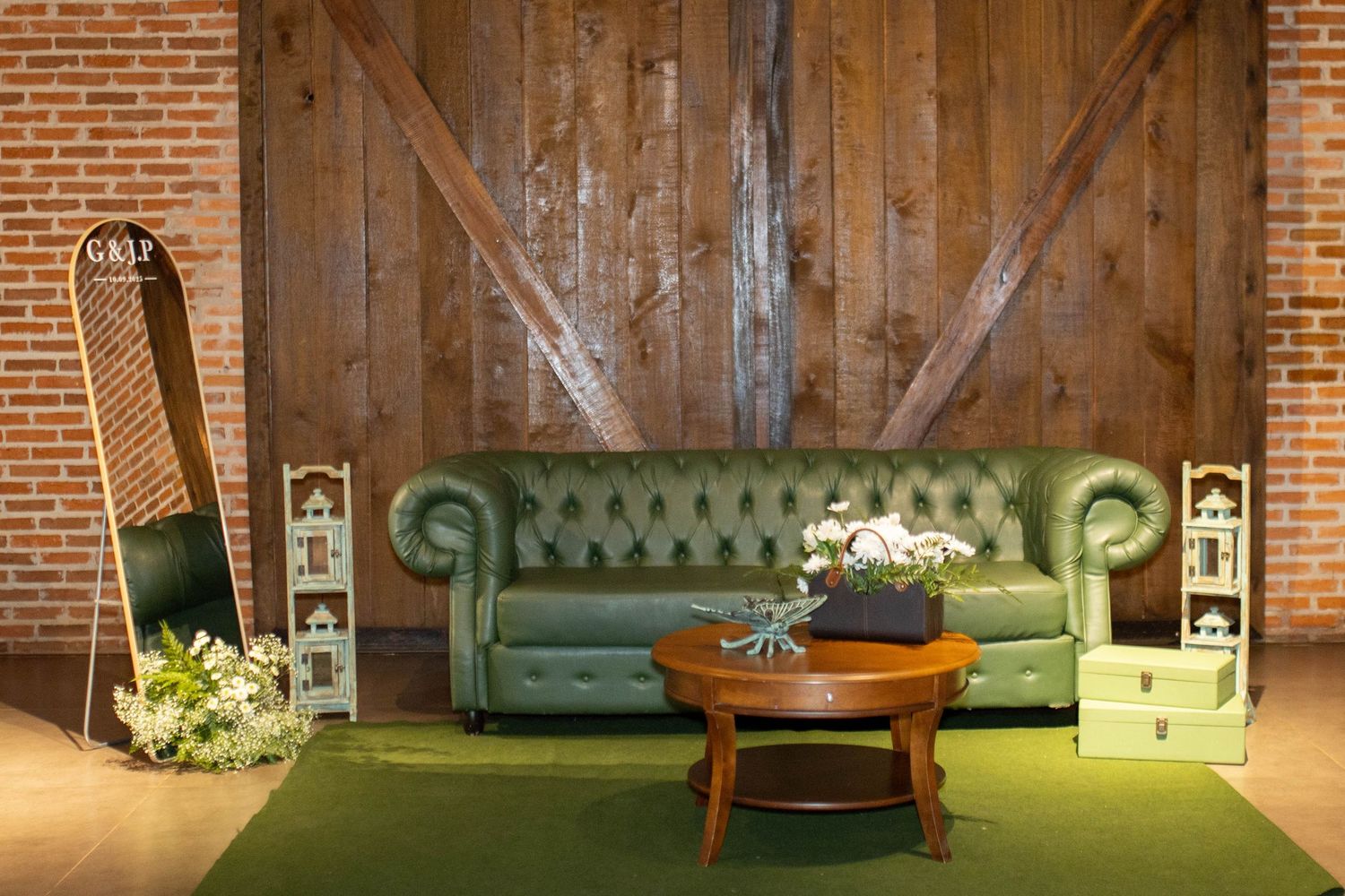Green tufted leather Chesterfield sofa with wooden coffee table on green rug against rustic barn wood wall.