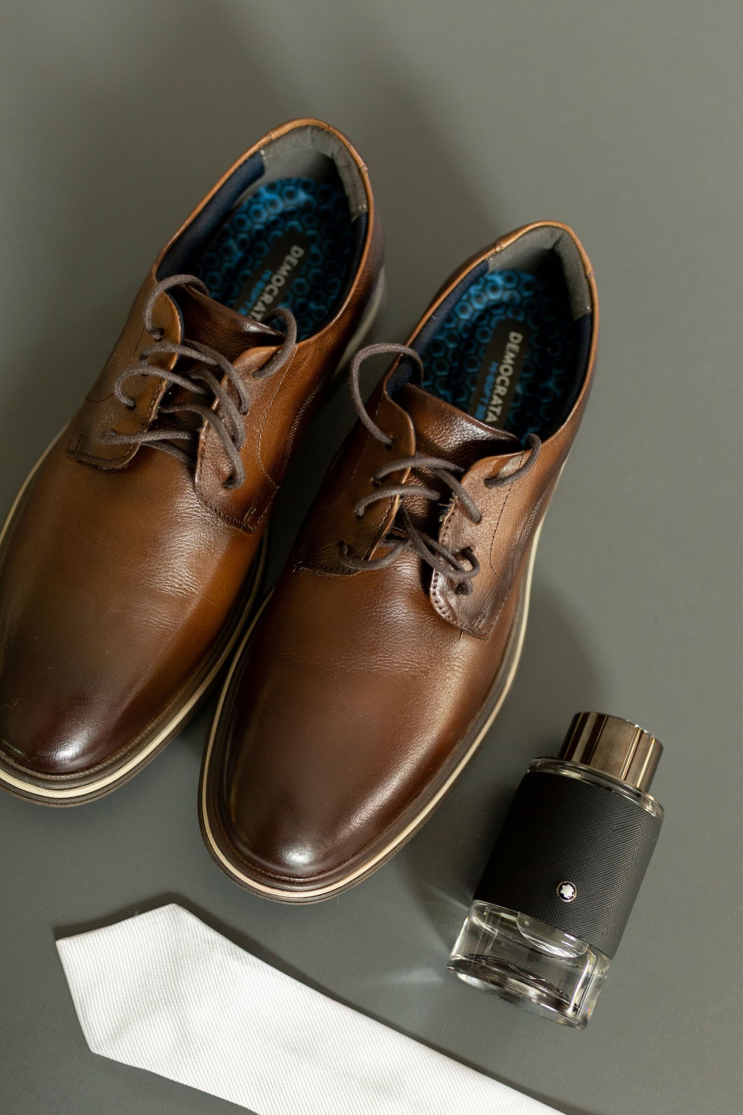 Brown leather derby shoes with white tie and Mont Blanc cologne on gray background, men's formal accessories.