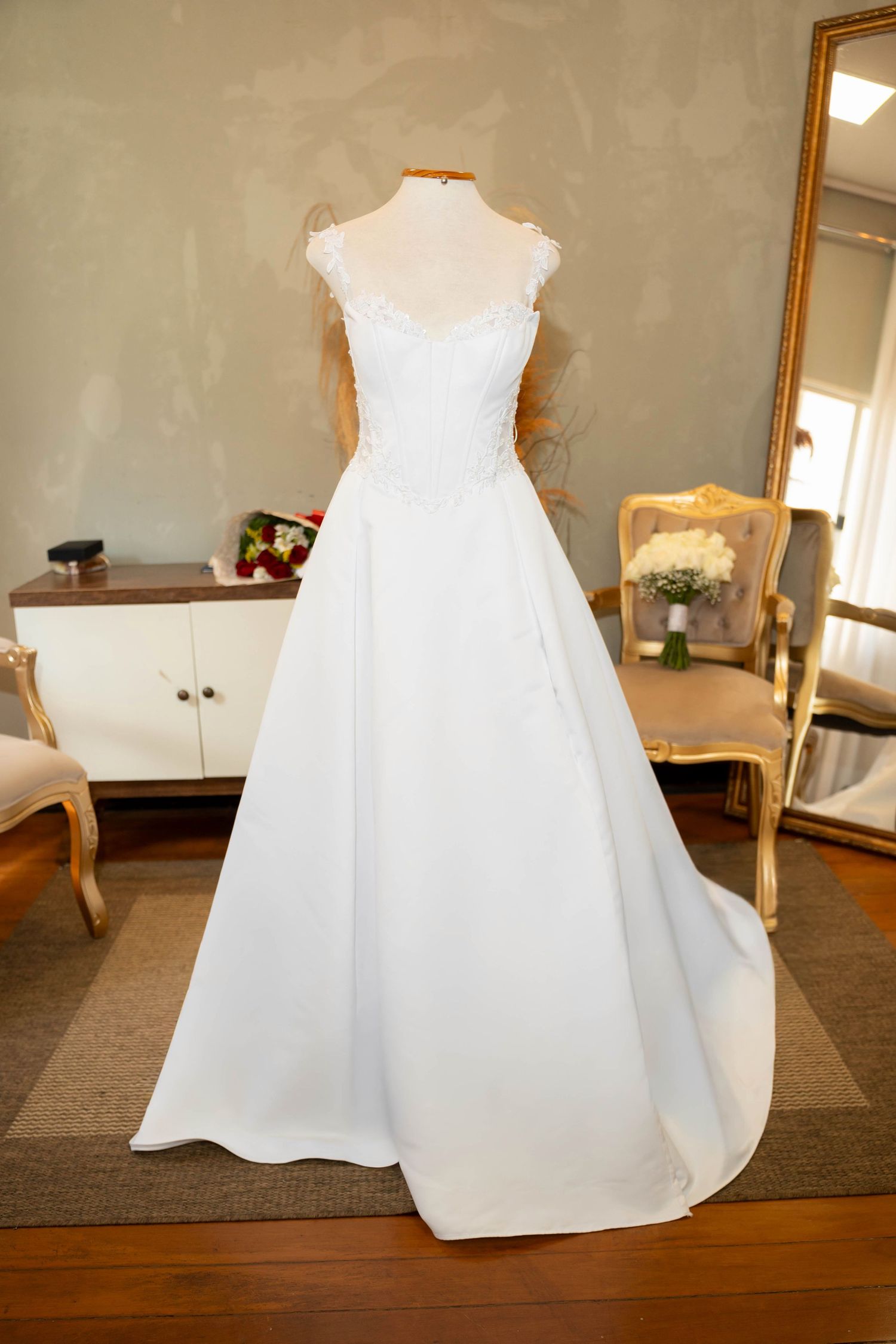 Elegant white A-line wedding dress with lace bodice and train displayed on mannequin in bridal boutique.