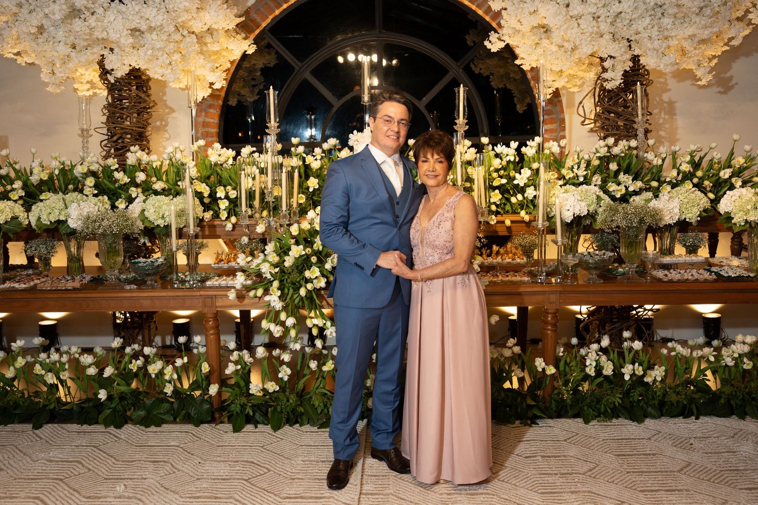 Elegant couple posing together at a wedding reception with white floral arrangements and candlelit decor.