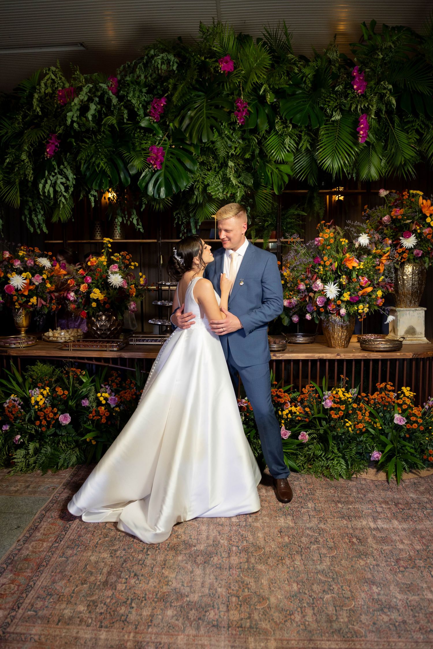 Bride and groom share first dance surrounded by lush tropical greenery and vibrant floral arrangements at elegant wedding reception.