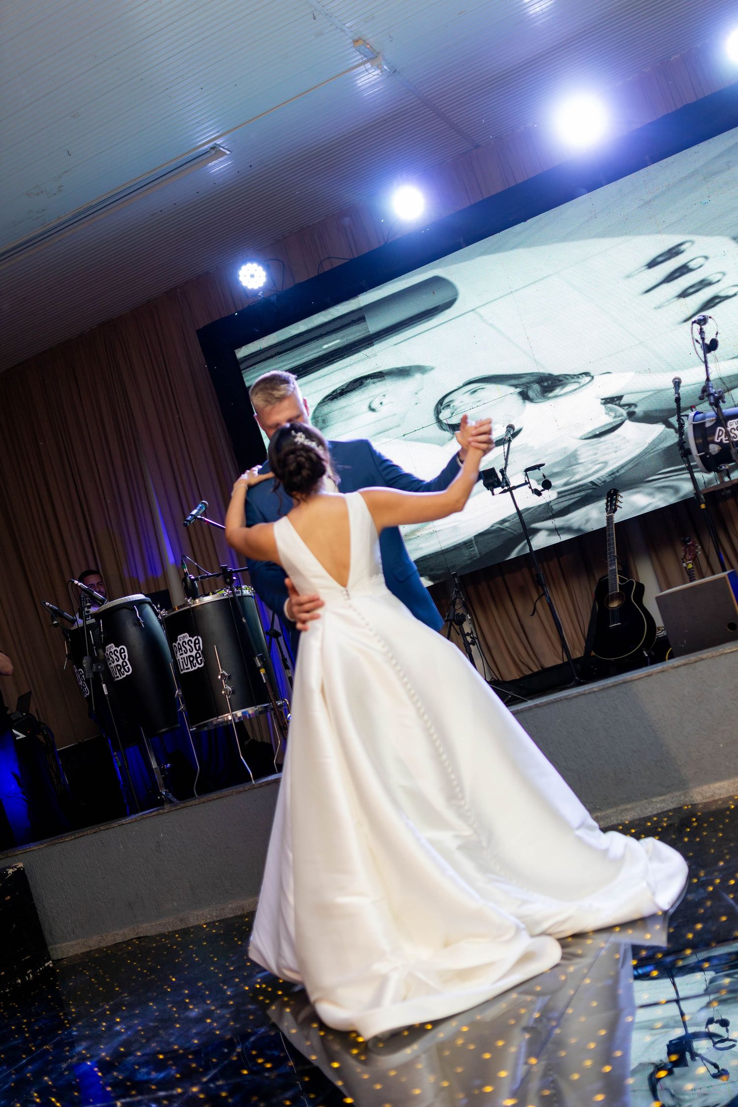 Bride and groom share their first dance at elegant wedding reception with live band and large screen backdrop.