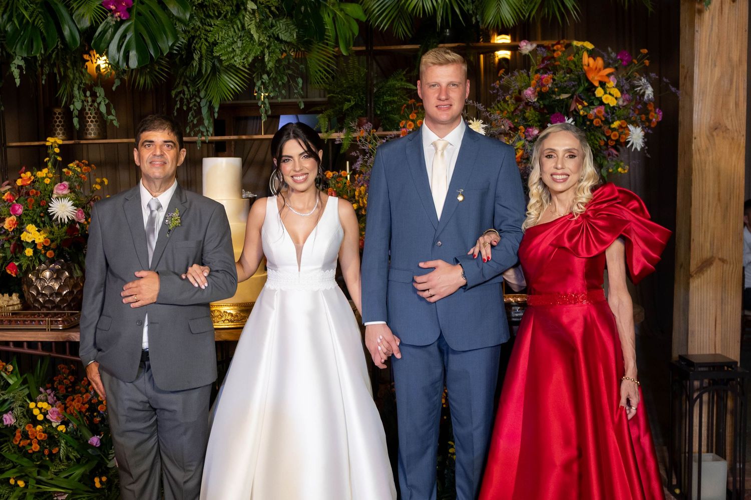 Wedding party poses with bride in white gown, groom in blue suit, man in gray suit, and woman in red dress.