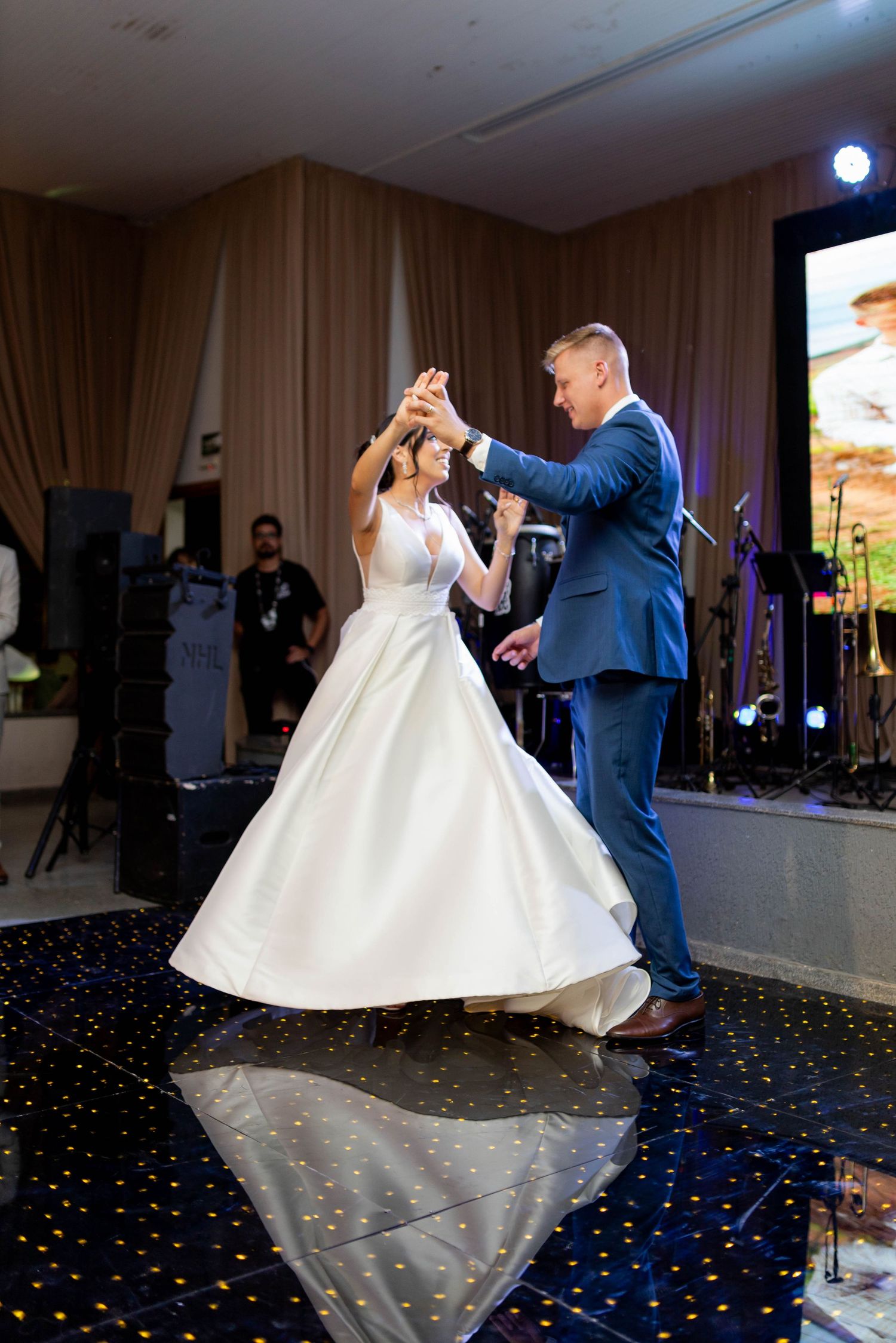 Bride and groom share their first dance at wedding reception, bride in white ballgown, groom in blue suit.