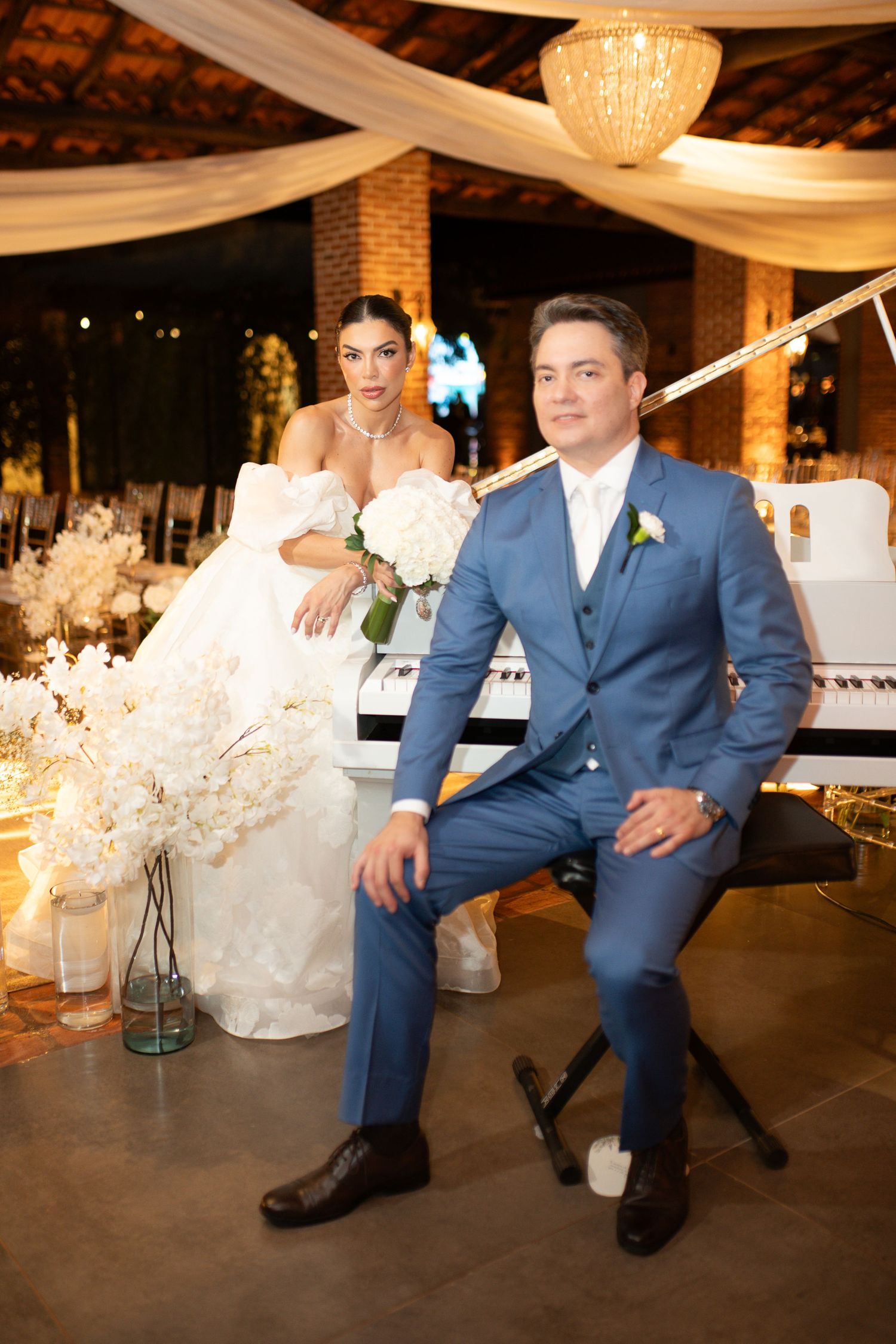 Elegant bride in white gown and groom in blue suit pose together at a romantic wedding reception venue.