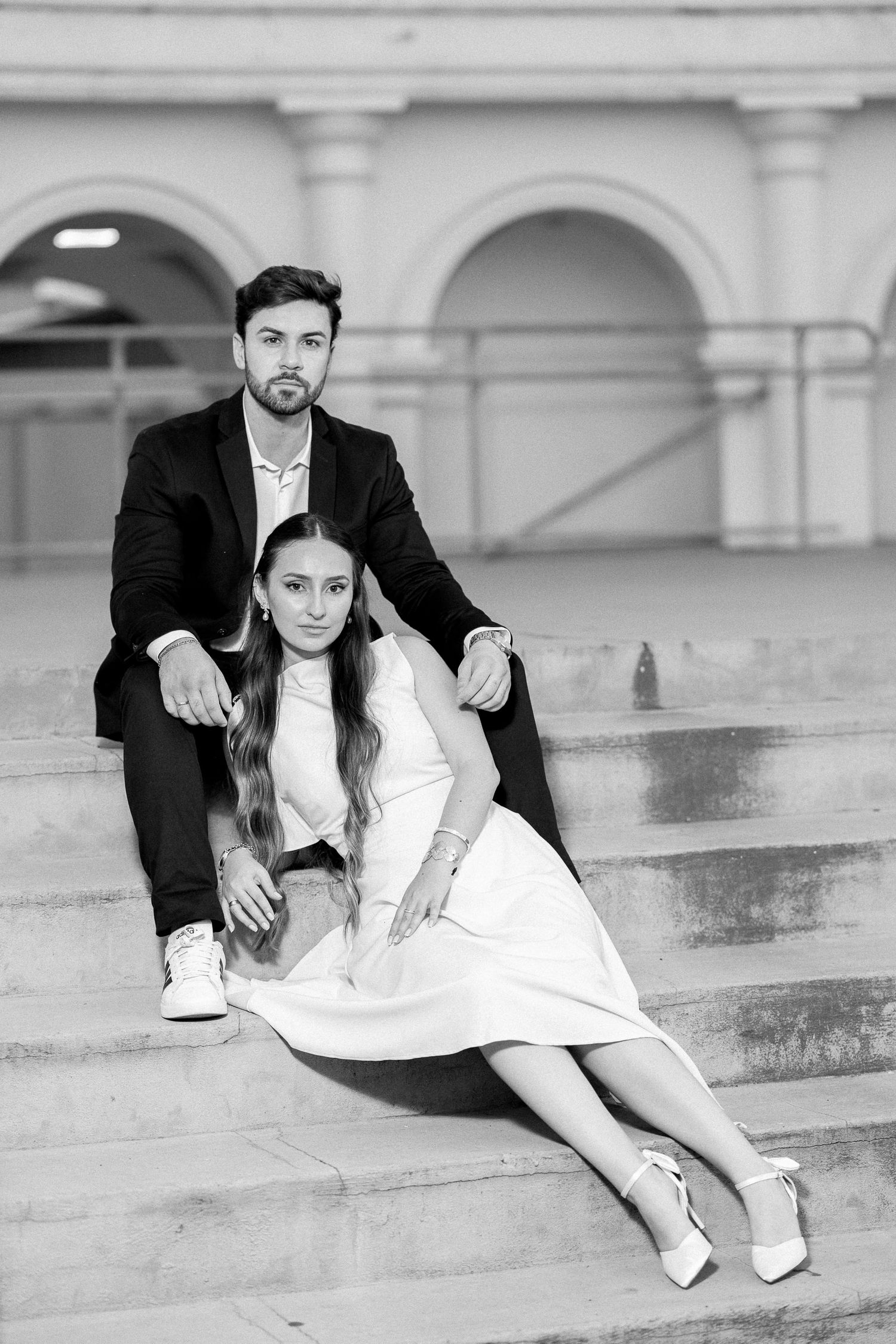 Black and white photo of an elegant couple sitting on stone steps outside a classical building.