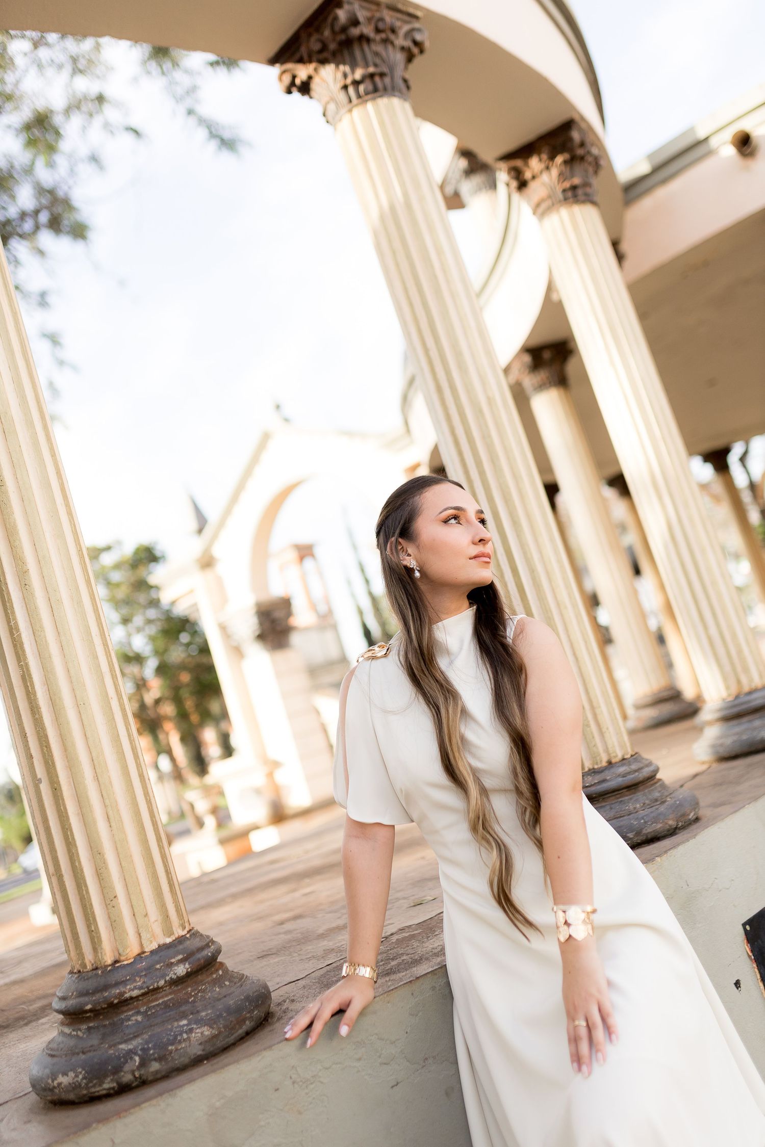 Elegant bride in white dress posing among classical Corinthian columns at an outdoor architectural monument.