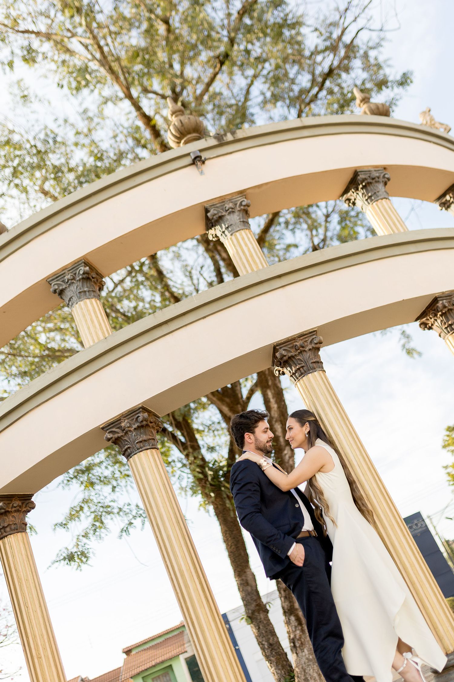 Bride and groom embrace under elegant classical arch with Corinthian columns outdoors on their wedding day.