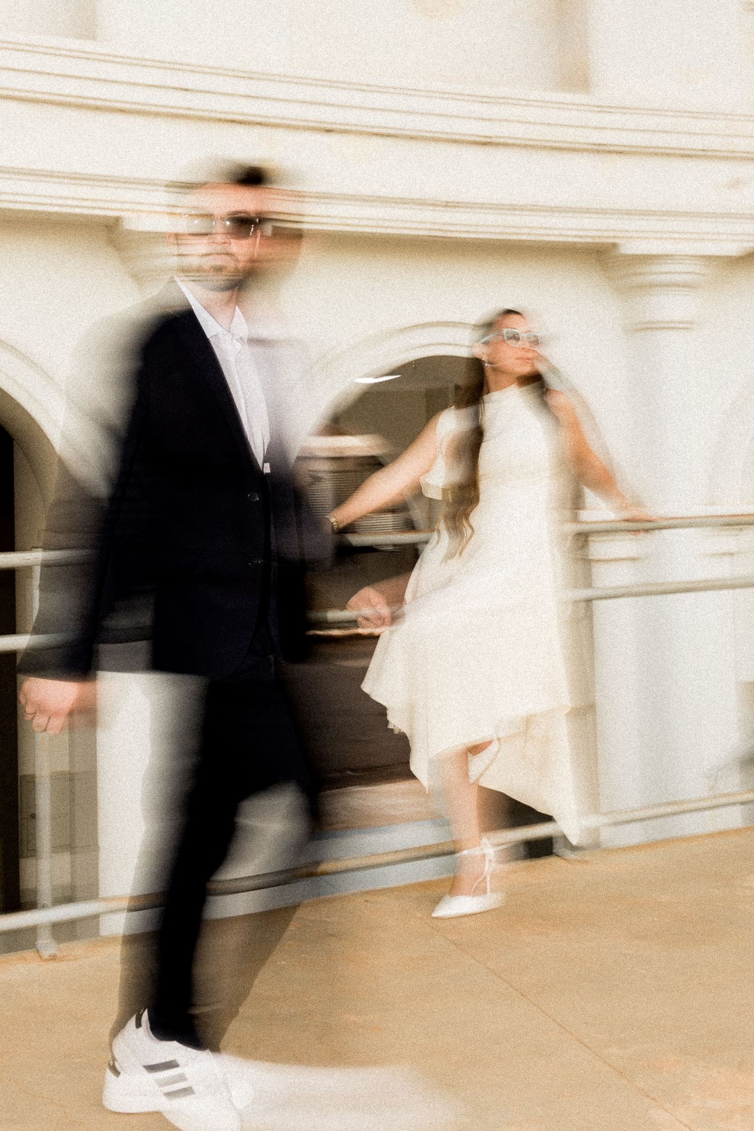 Bride and groom in sunglasses with artistic motion blur effect at elegant white classical building.