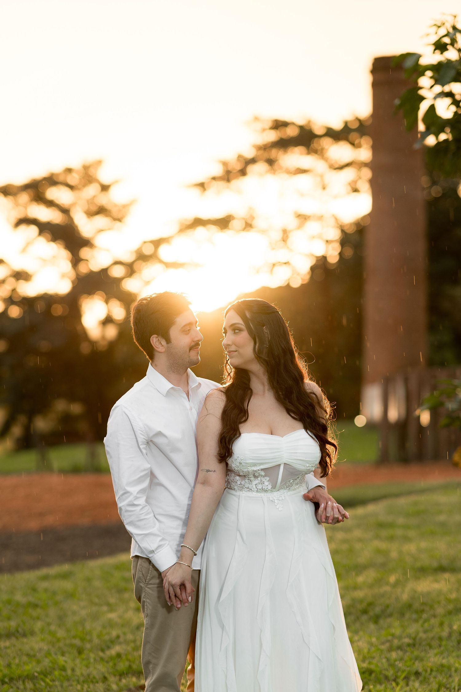 Romantic couple in wedding attire sharing a tender moment at golden sunset near brick tower.