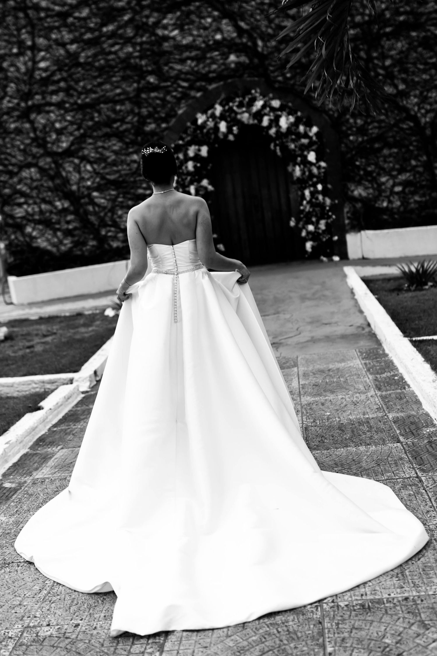 Bride in strapless white ballgown with long train walks toward arched doorway in black and white wedding photo.