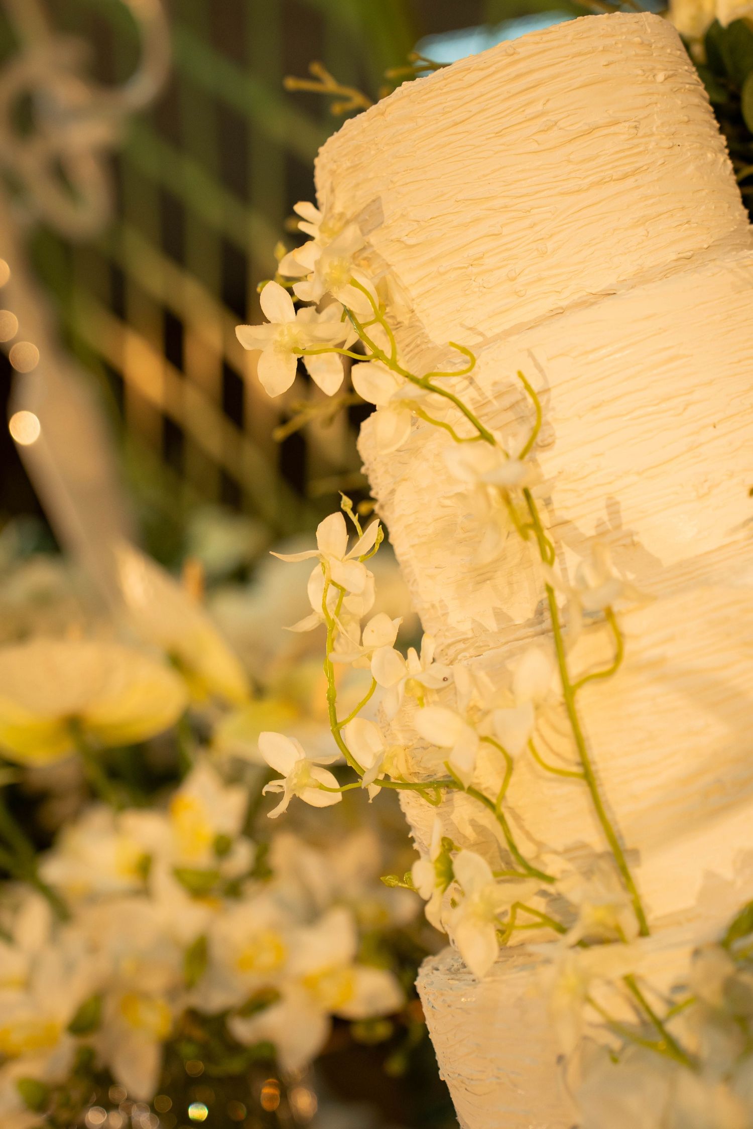 Elegant white wedding cake with delicate orchid flowers cascading down tiered layers at a formal event.