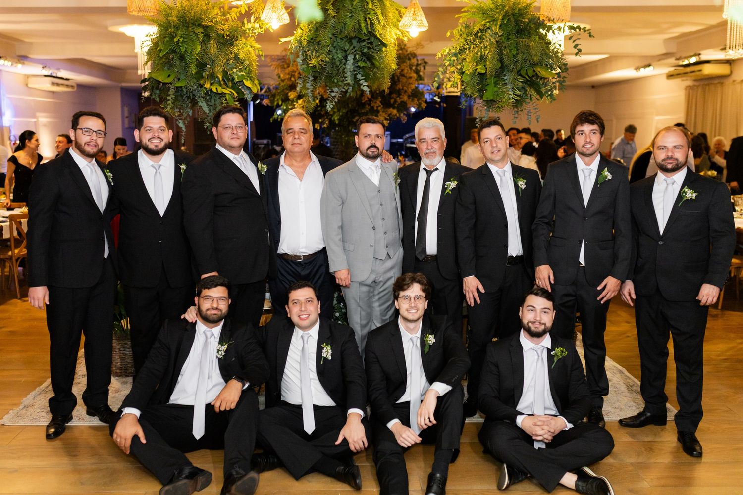Group of men in formal black suits posing together at an elegant wedding reception venue.