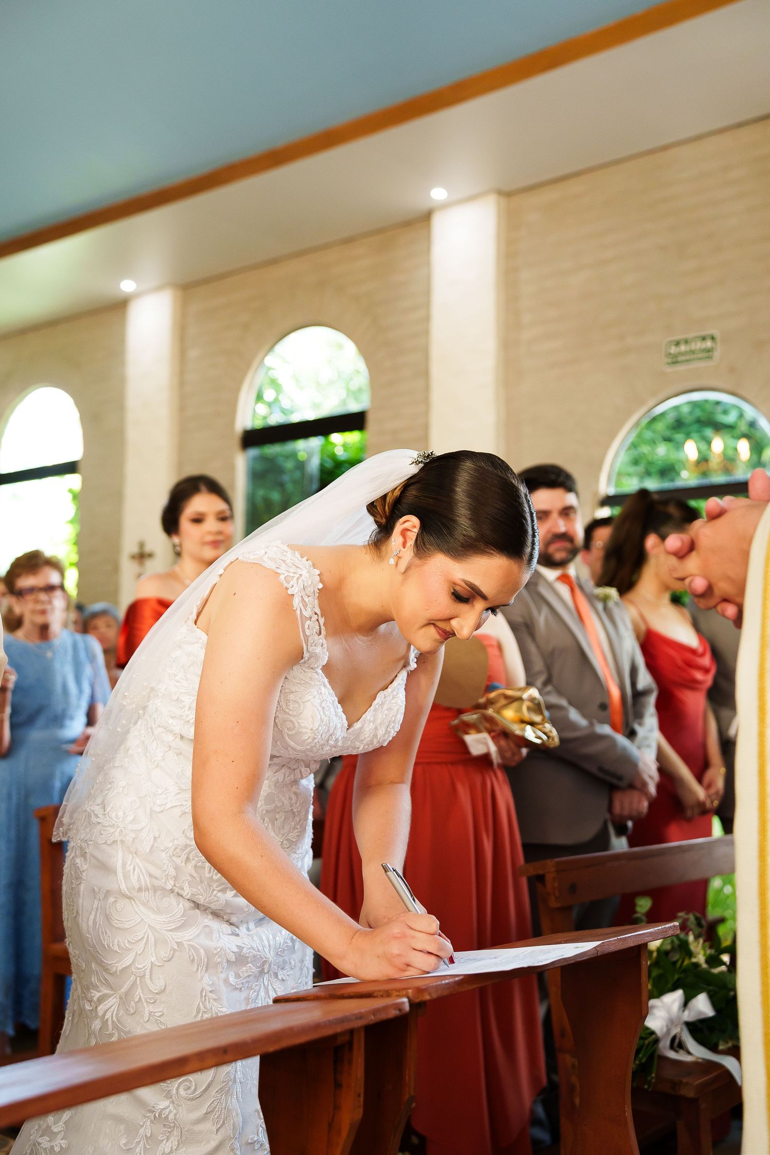 Bride in white lace gown signing marriage certificate at church altar during wedding ceremony.