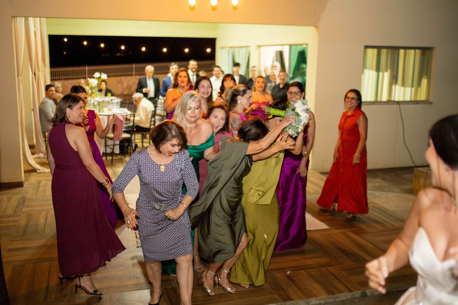 Guests dancing and celebrating at a wedding reception in a warmly lit venue with colorful formal attire.