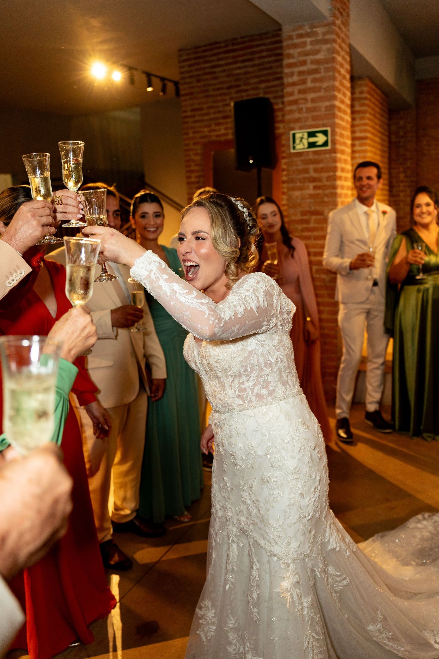 Bride in white lace gown toasting champagne with guests at wedding reception, smiling joyfully.