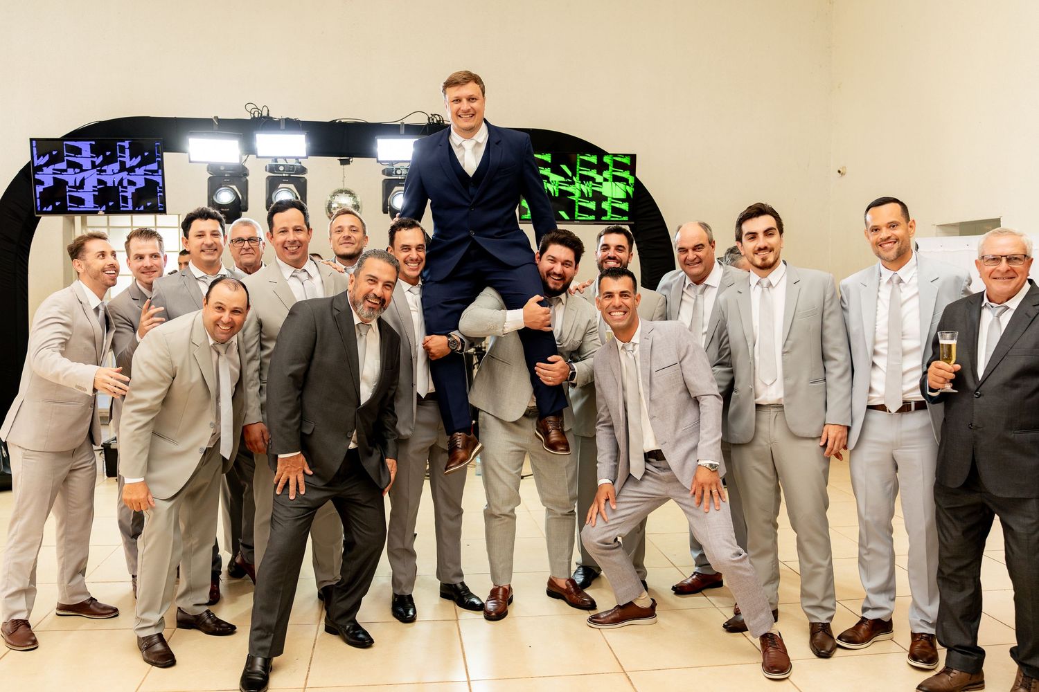 Groomsmen in gray suits celebrate by lifting the groom at a wedding reception photo.