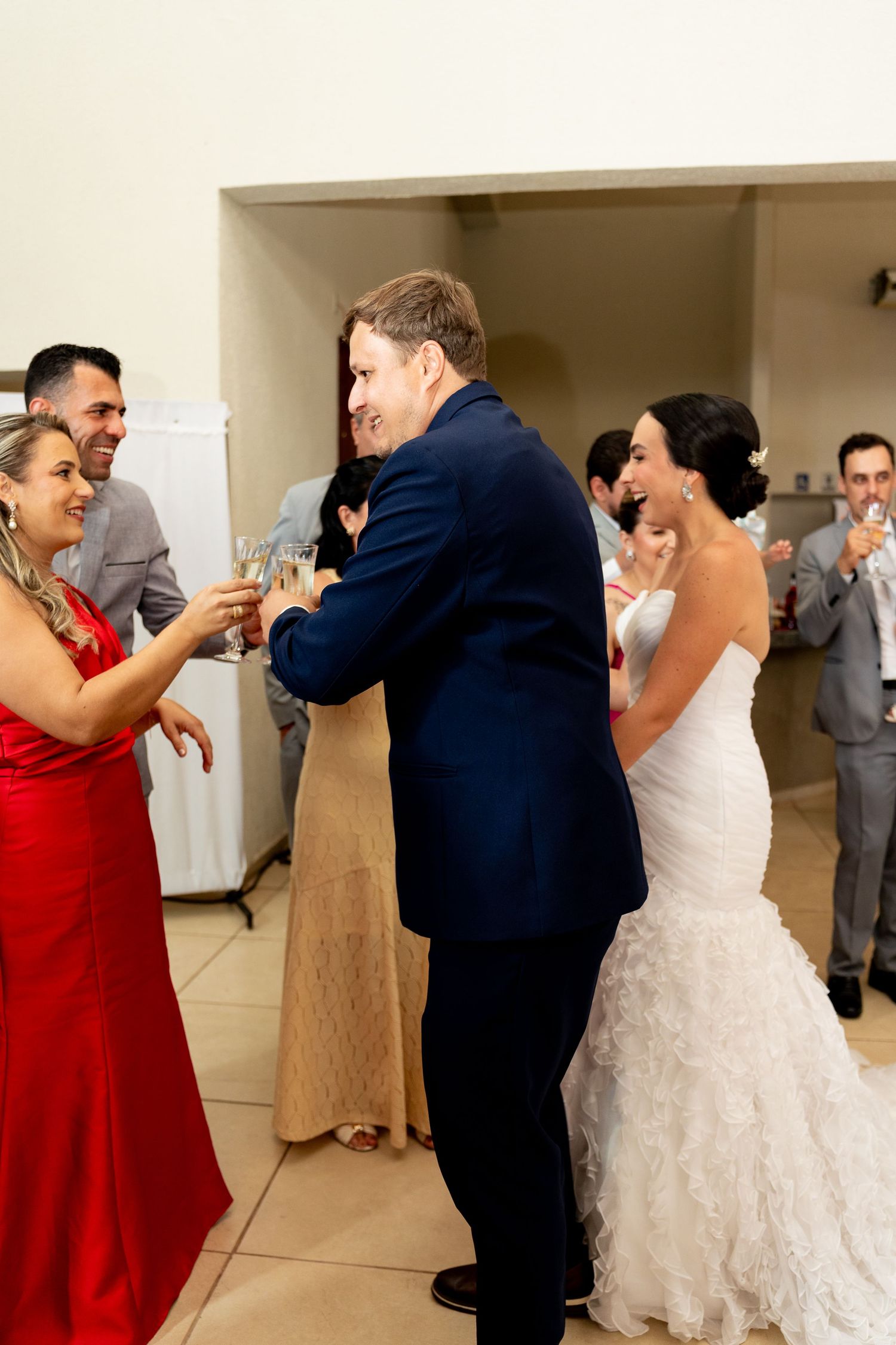 Bride in white gown and groom in navy suit toast champagne with guests at wedding reception.