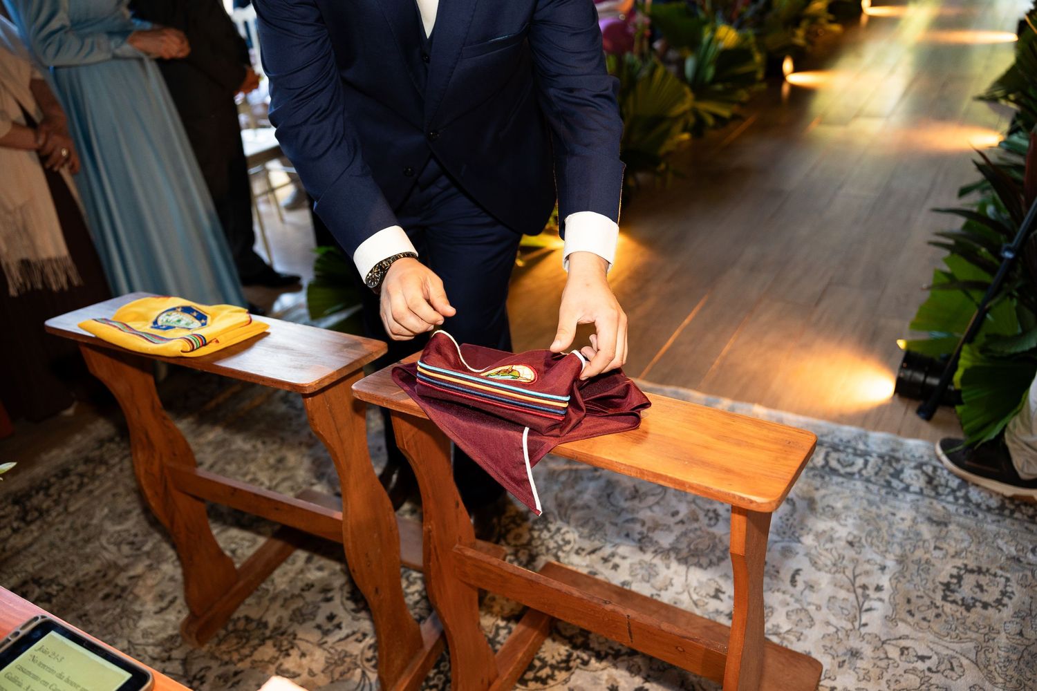 Man in suit folding a burgundy ribbon on a wooden table at a wedding ceremony.